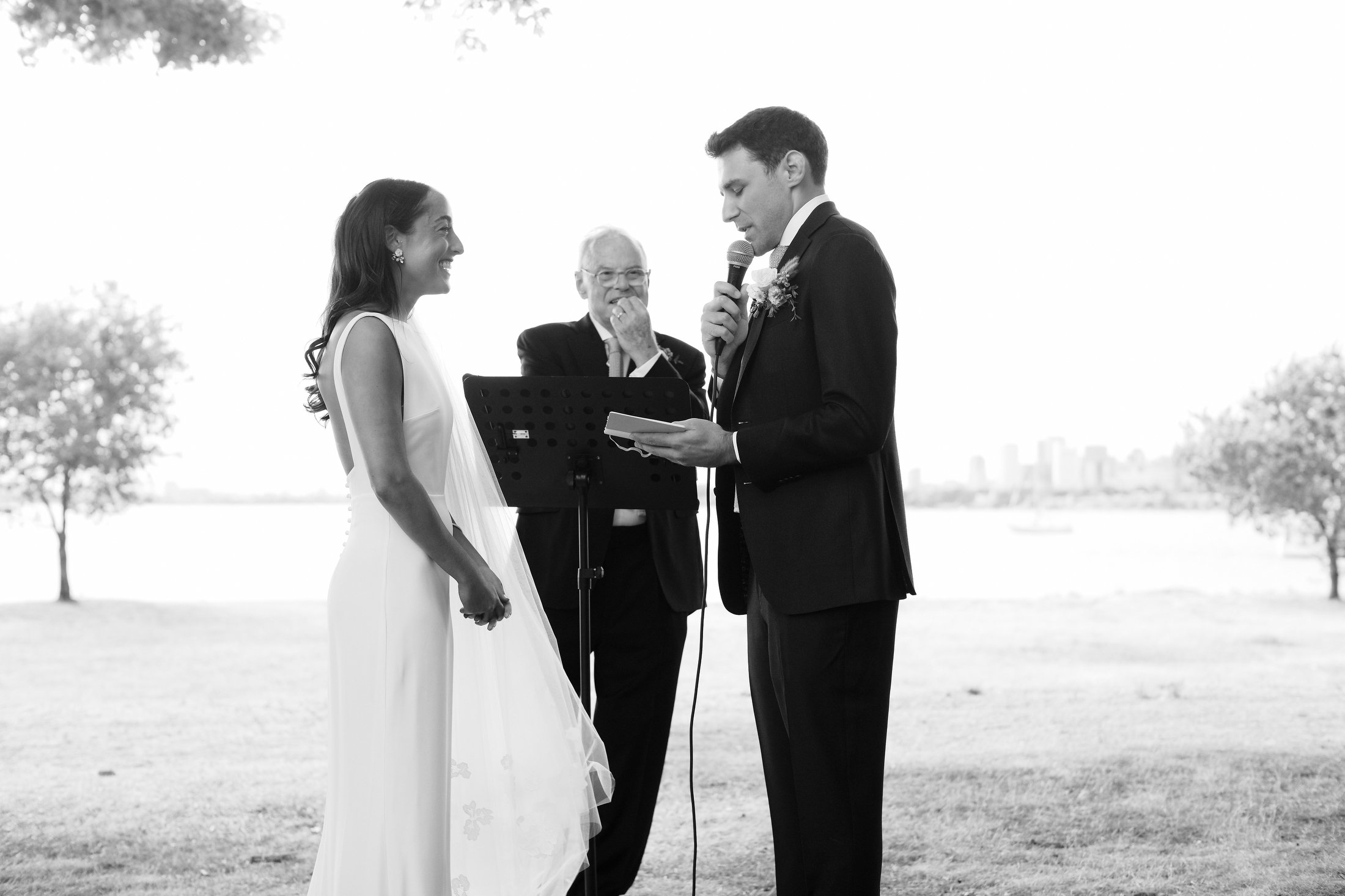 A couple getting married outdoors with an officiant, with a city skyline in the background.