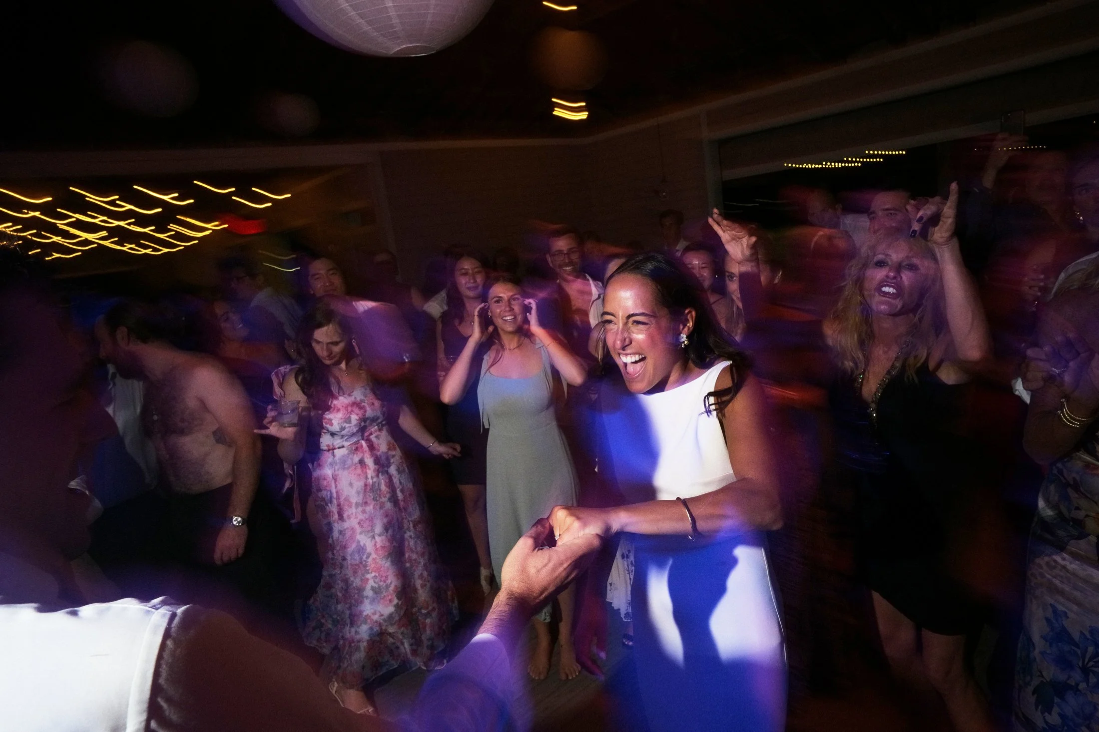 People dancing and celebrating at a party with colorful lights and joyful expressions.
