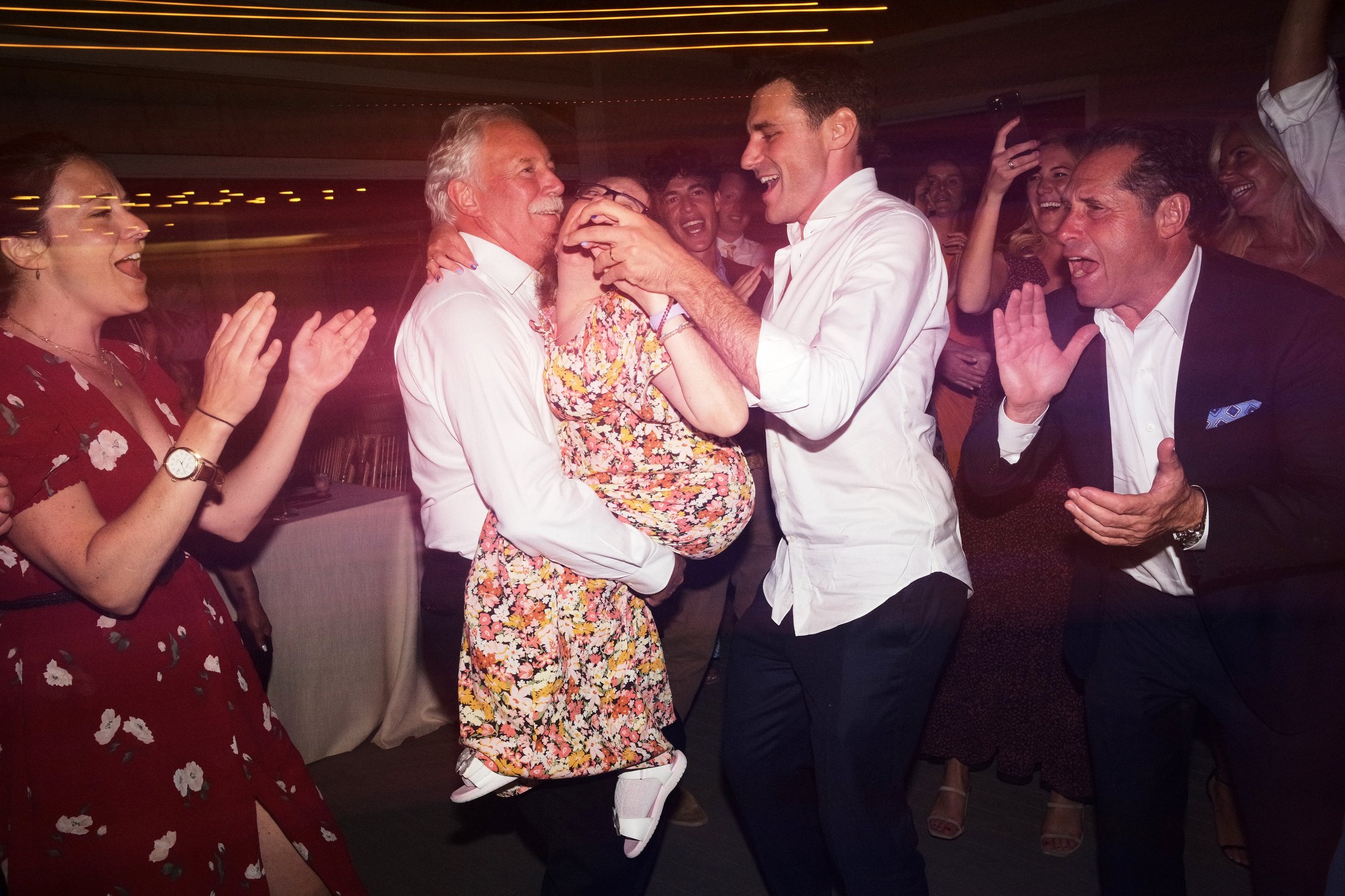Group of people dancing and celebrating at an indoor party, with joyful expressions and colorful lighting.