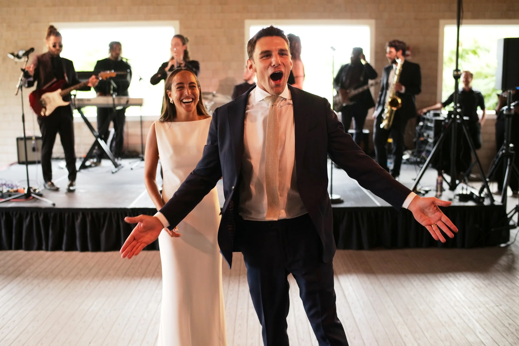A joyful couple dancing at a wedding reception with a live band playing on stage in the background.