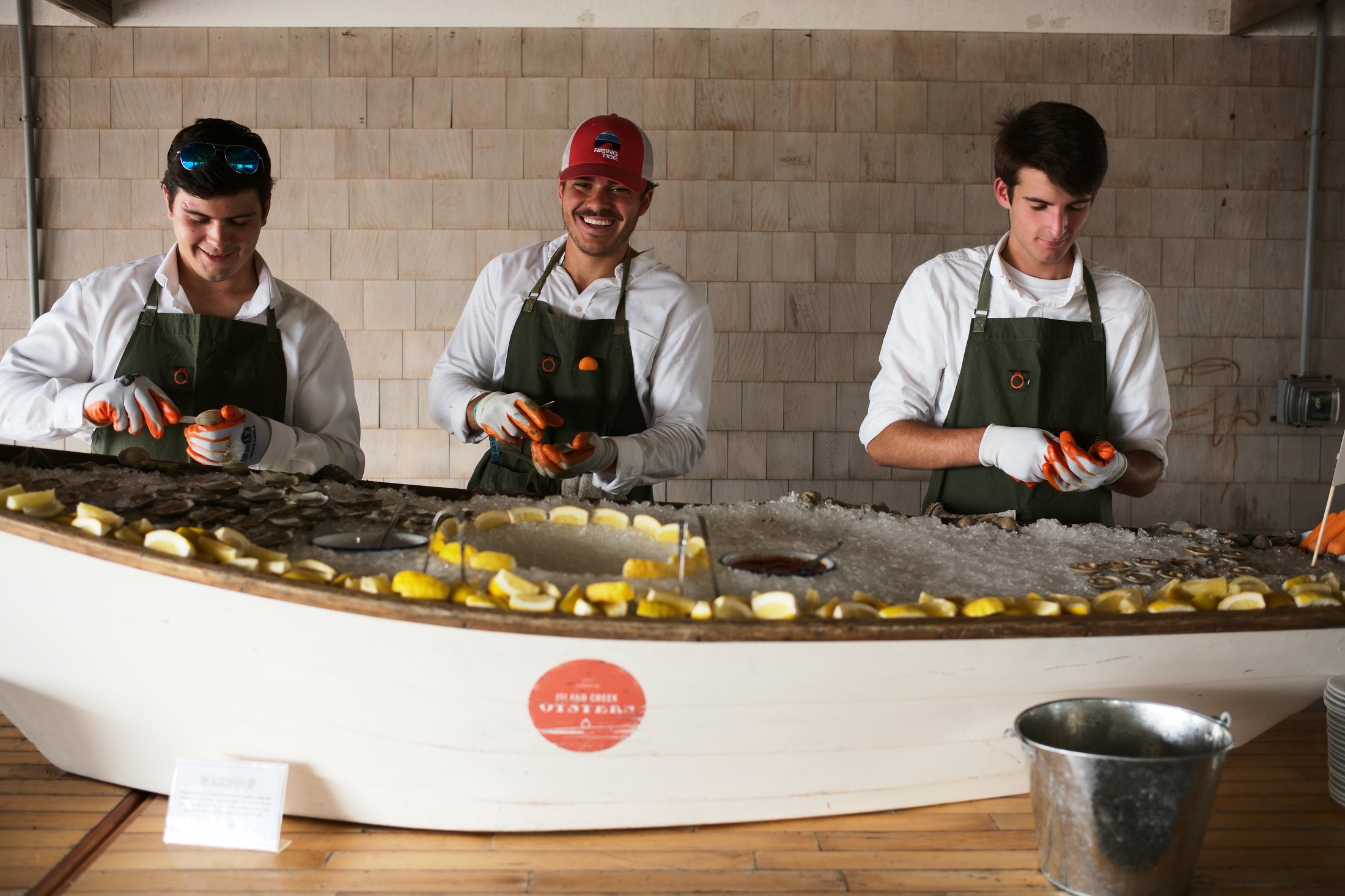 Three young men working at a seafood bar peeling and preparing oysters, with lemon slices on display in front of them