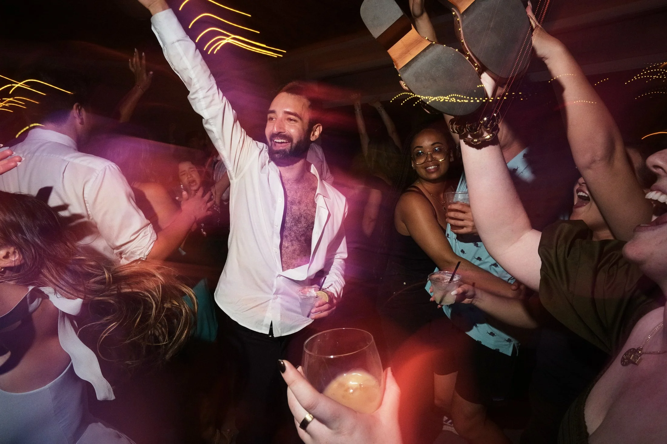 People dancing and celebrating at a party with drinks in hand and colorful lights.