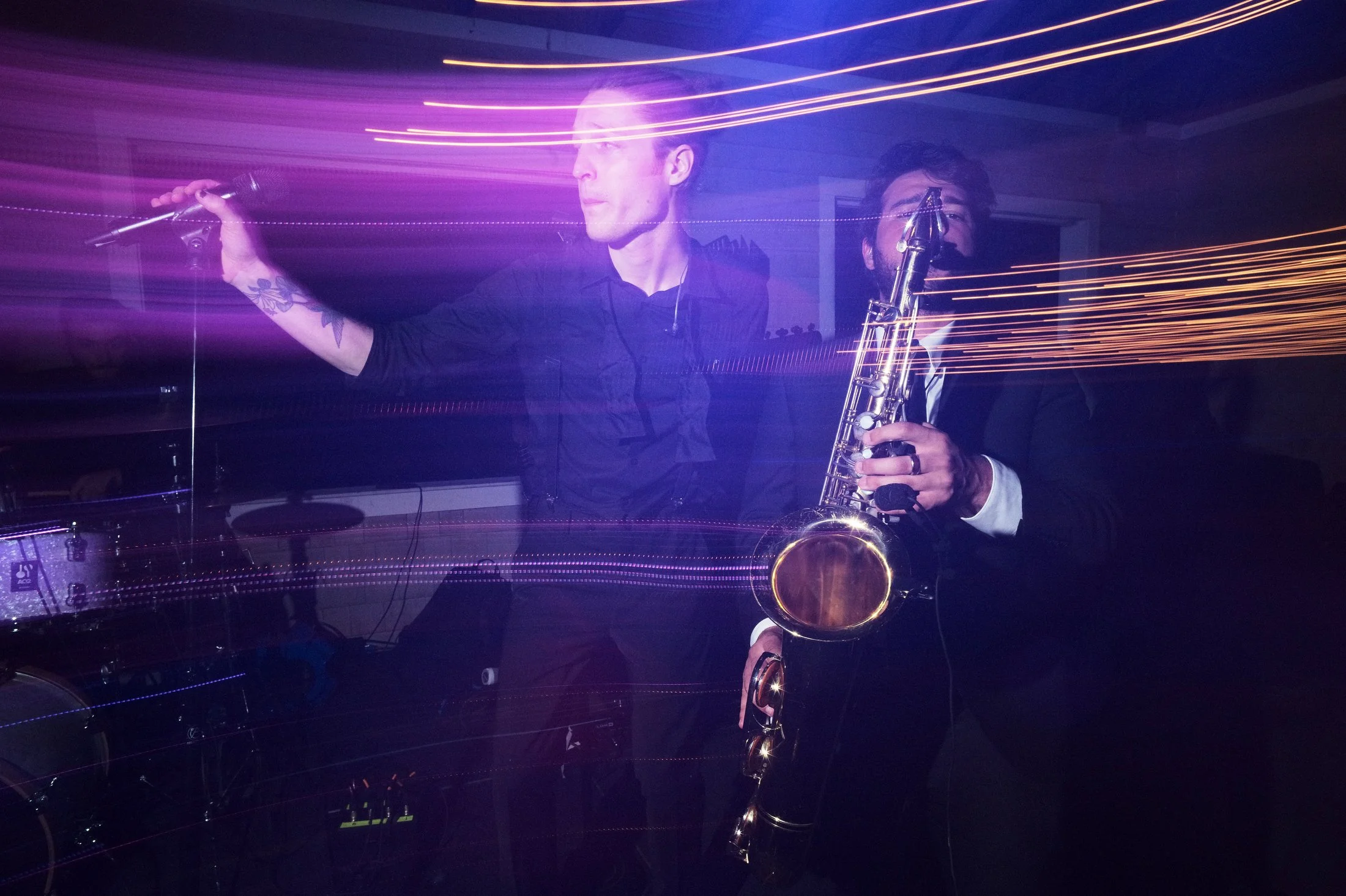 Two musicians performing with light streaks in the background, one holding a microphone and the other playing a saxophone.