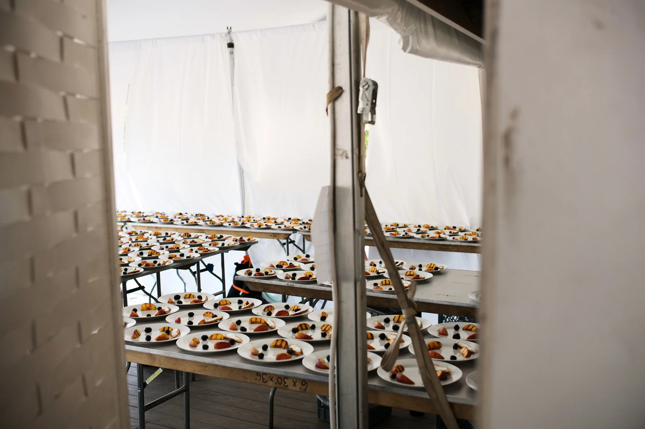 Plates of food lined up on tables inside a white tent.