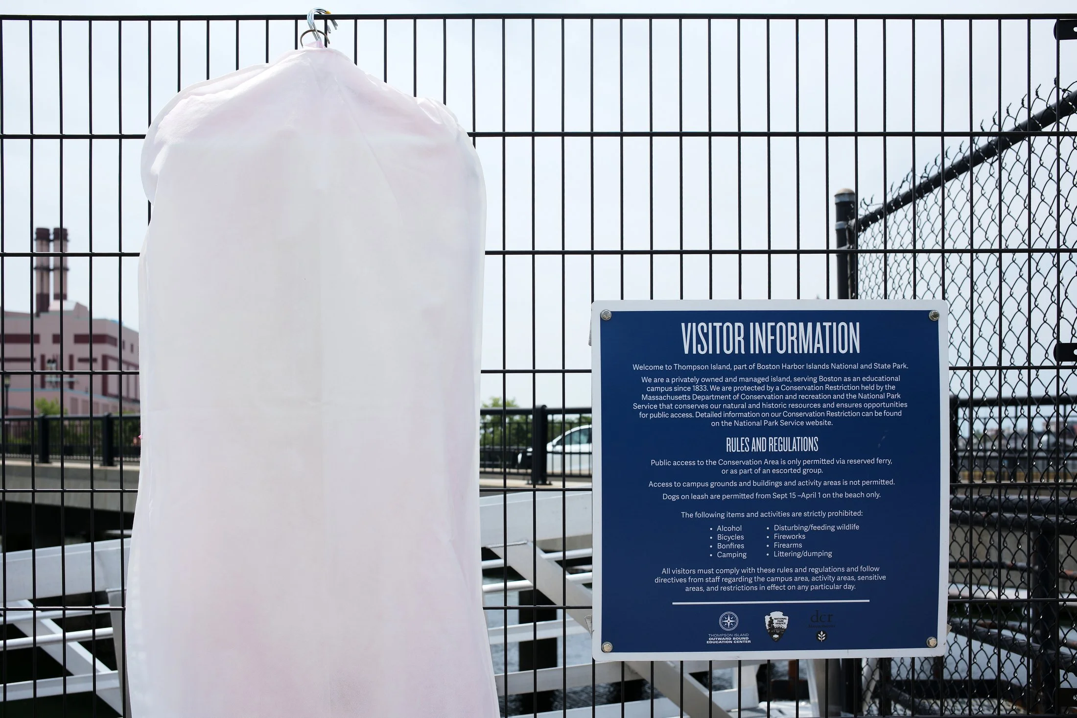 Visitor information sign on a fence at Thompson Island, part of Boston Harbor Islands National and State Park, with a blank white cover on a hanger next to the sign.