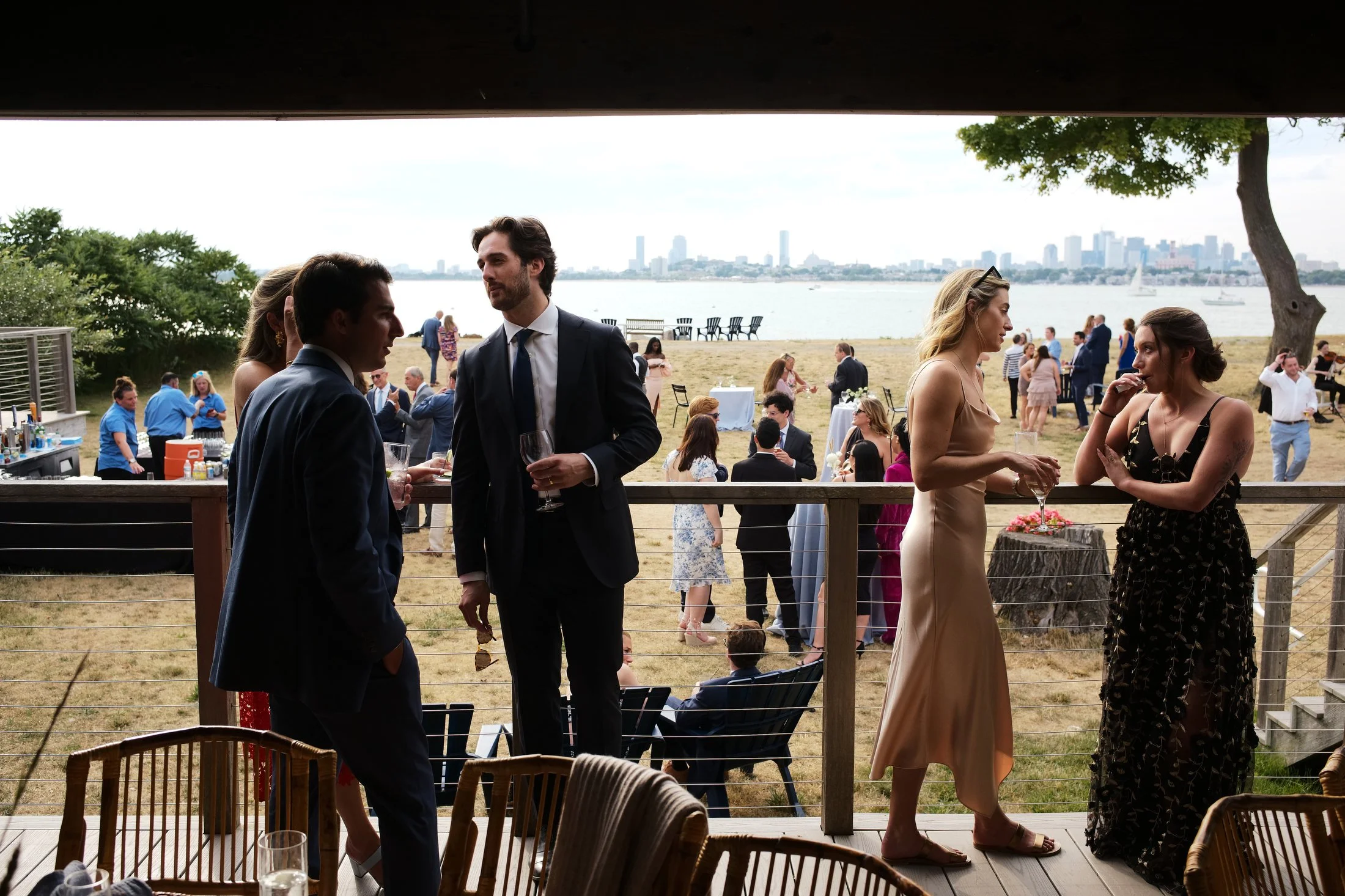 People socializing at an outdoor waterfront event with city skyline in the background.