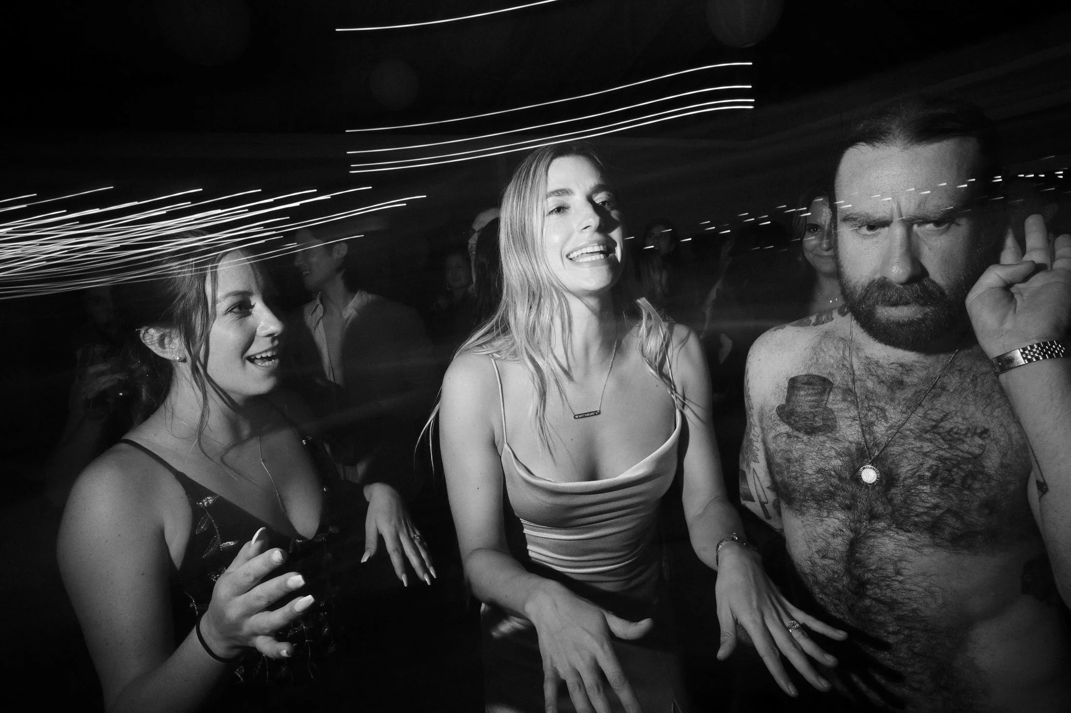 People dancing at a party or club, with light streaks overhead, in black and white.