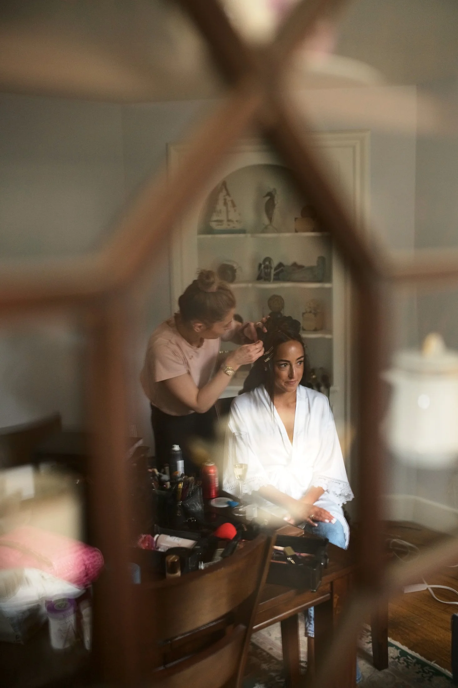 A woman sitting on a chair while getting her hair styled by a hairstylist in a room seen through a decorative mirror frame.