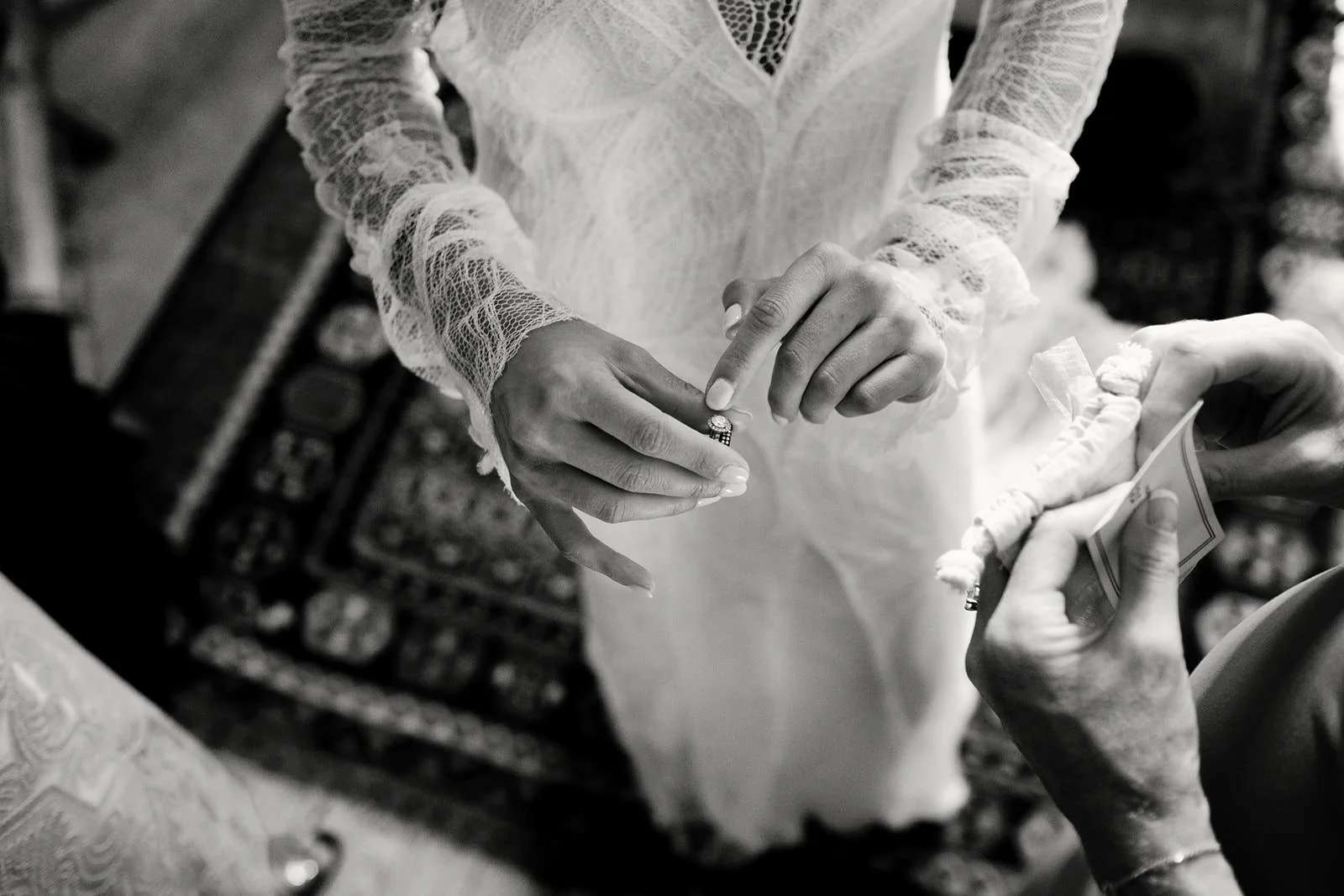 A bride wearing a lace wedding dress placing a ring on her finger during a wedding ceremony.