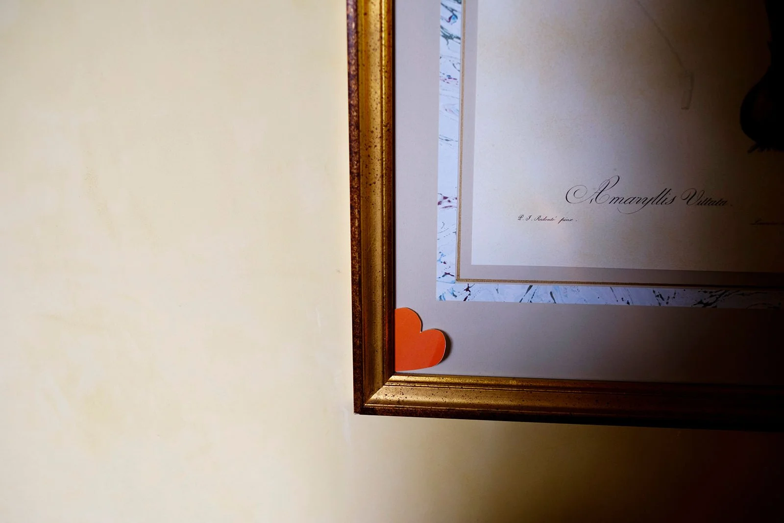 Close-up of a decorative framed certificate or artwork with a small orange paper heart in the bottom left corner.