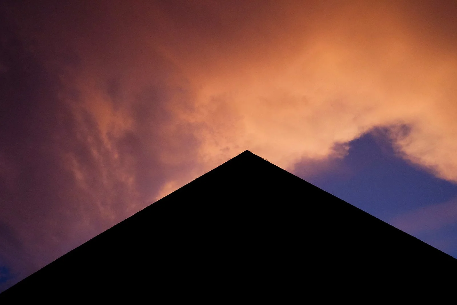 Silhouette of a building's roof against a colorful sky with pink and purple clouds