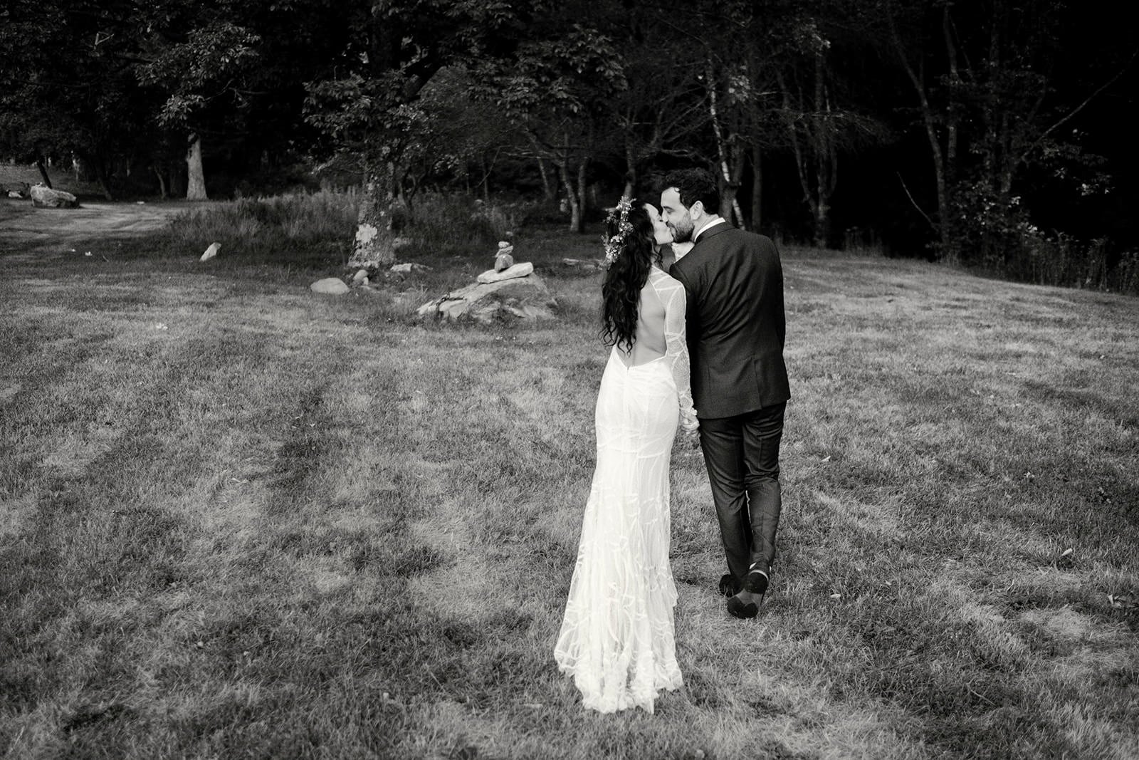 A bride and groom kissing in an outdoor setting with grass and trees in black and white.