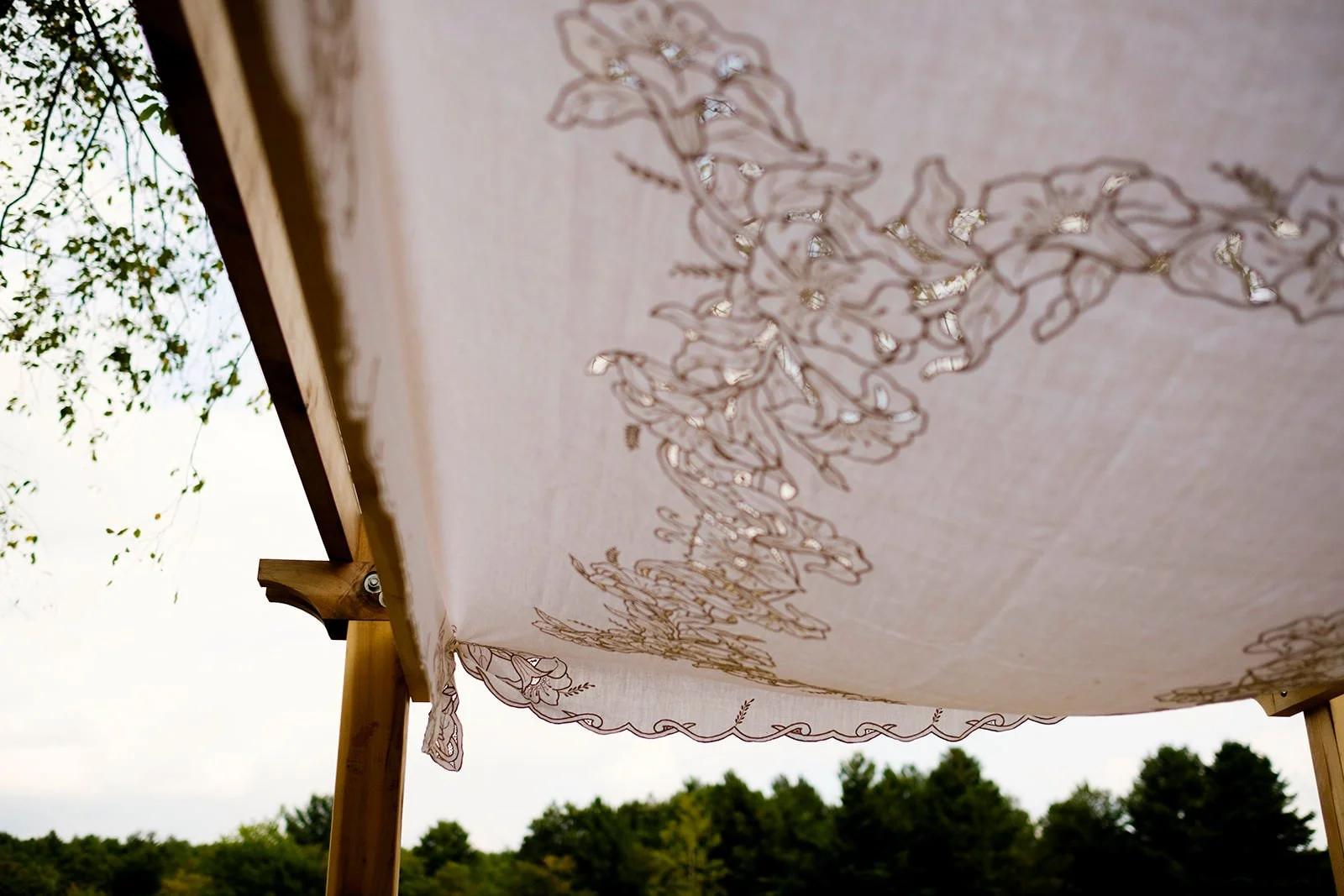 A close-up view of a decorative hanging fabric with embroidered floral patterns, outdoors with trees and sky in the background.