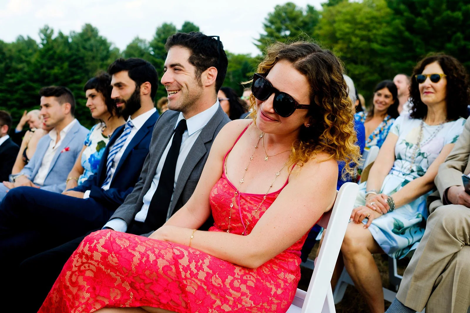 People seated outdoors at a wedding ceremony, smiling and enjoying the event.