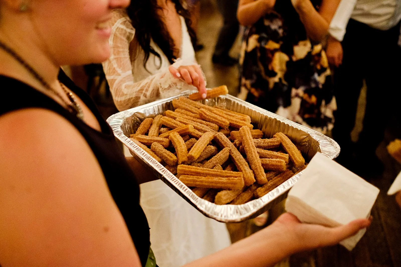 A woman holding a tray of churros at a social gathering.