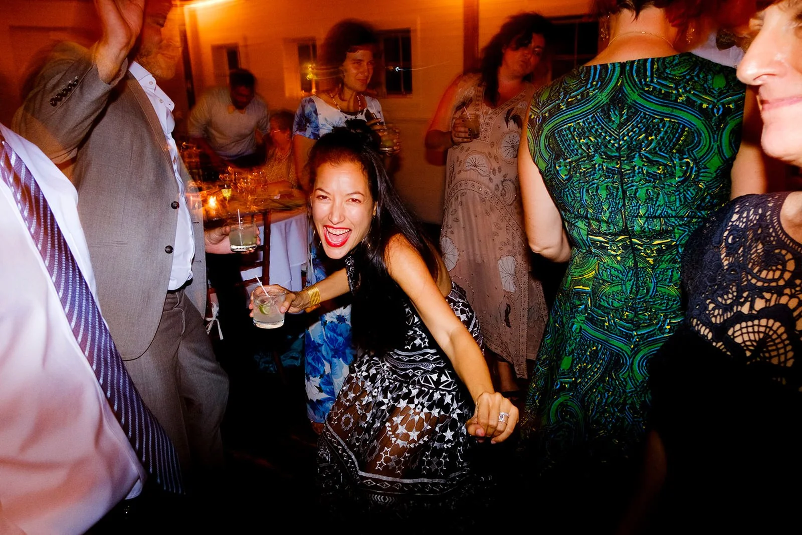 People dancing and socializing at a lively party with drinks and colorful attire.