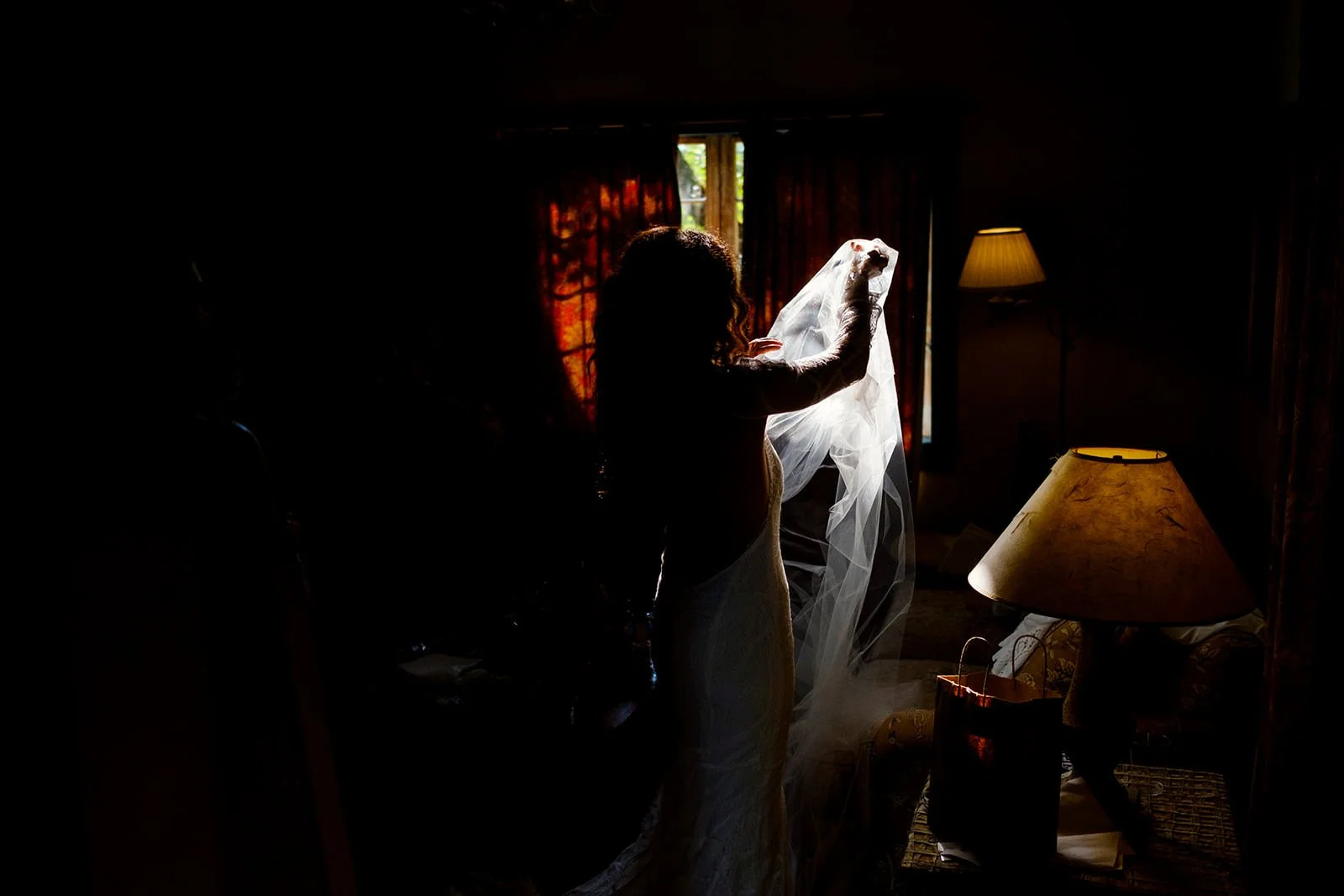 A woman is holding a wedding veil in a dark room with some light coming from a window