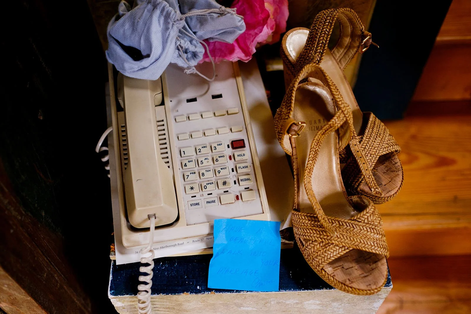 A beige rotary phone, a pair of tan high-heeled sandals, a blue note, and some clothing items on a small table.