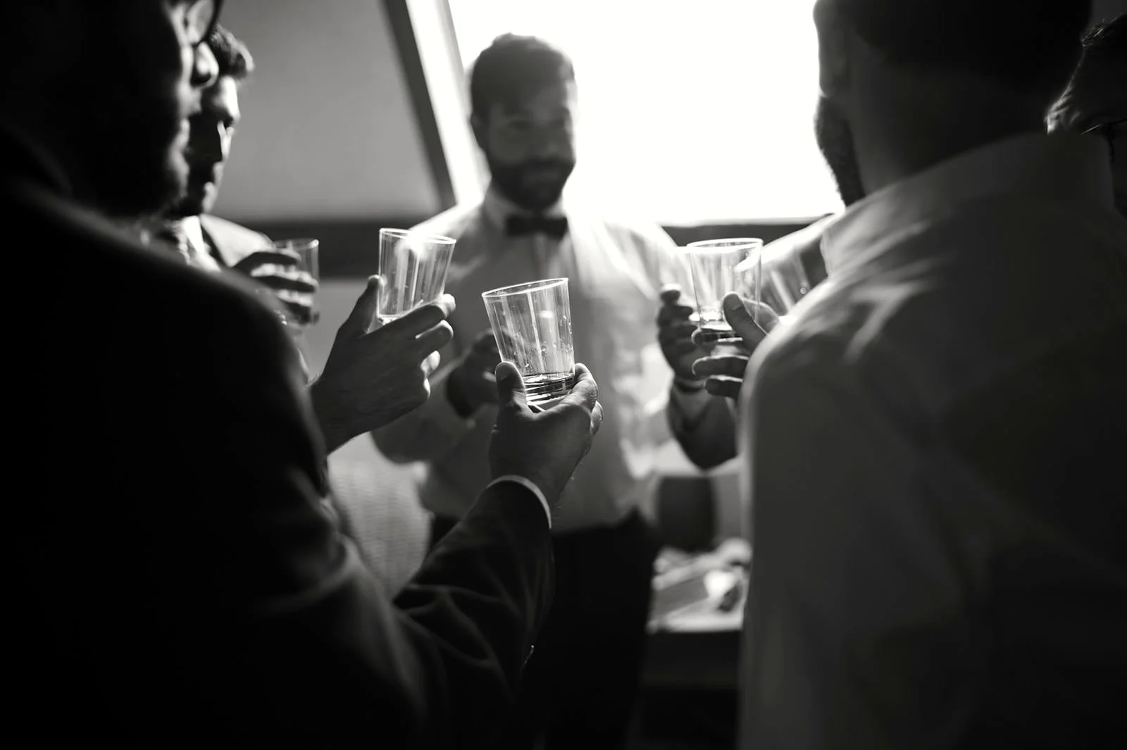 Group of men wearing formal attire raising glasses in a toast in a well-lit indoor setting.