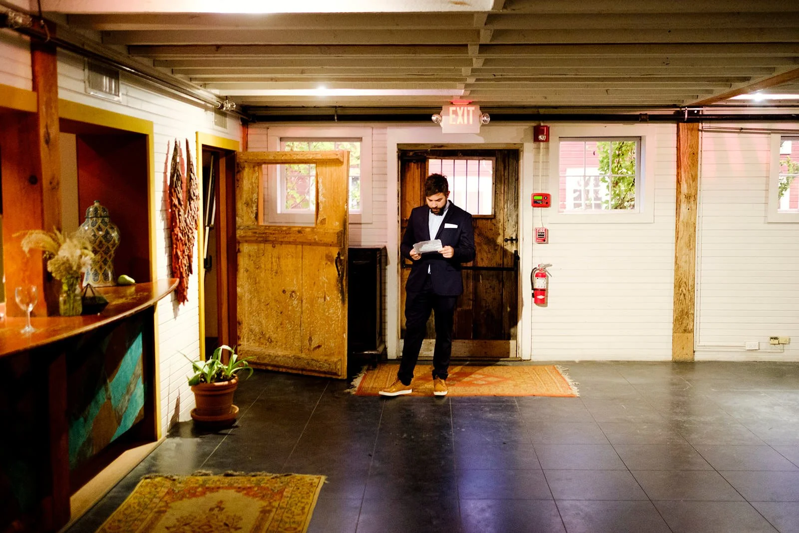 Man in a dark suit reading a paper in a rustic-style interior space with wooden doors, windows, and a reception area.