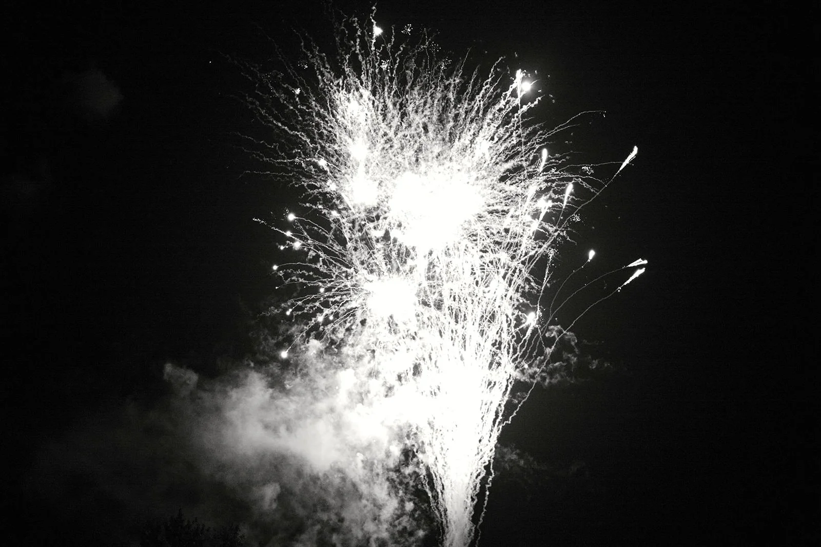 Black and white photo of fireworks exploding in the night sky.