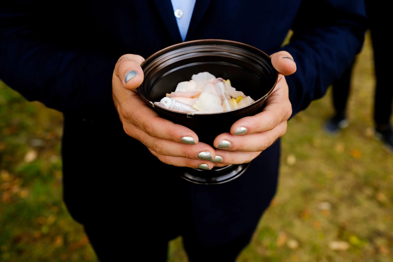 Person holding a black bowl filled with medical supplies, including syringes, in an outdoor setting.