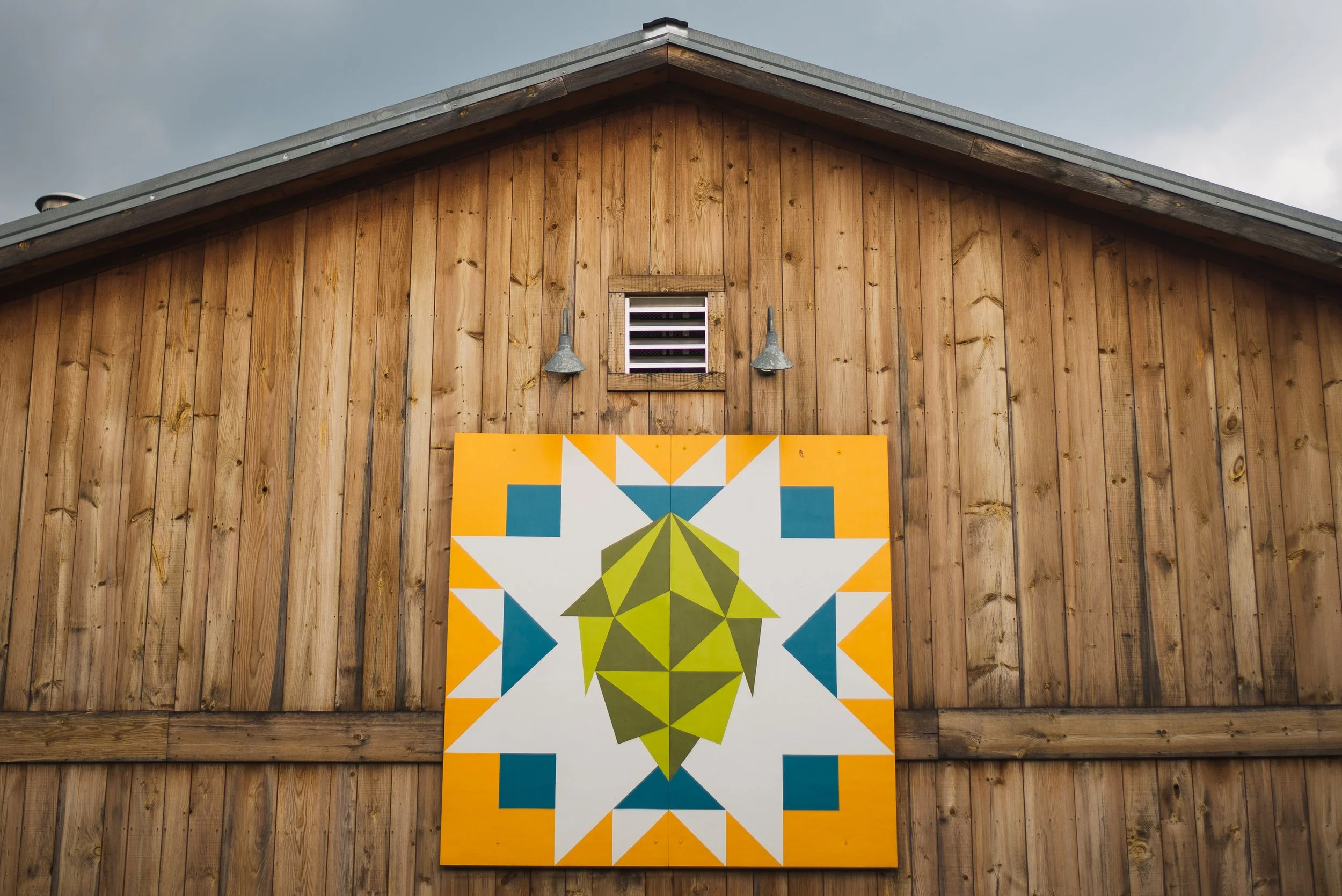 Wooden barn exterior with small window, two wall-mounted lights, and a colorful geometric art piece.