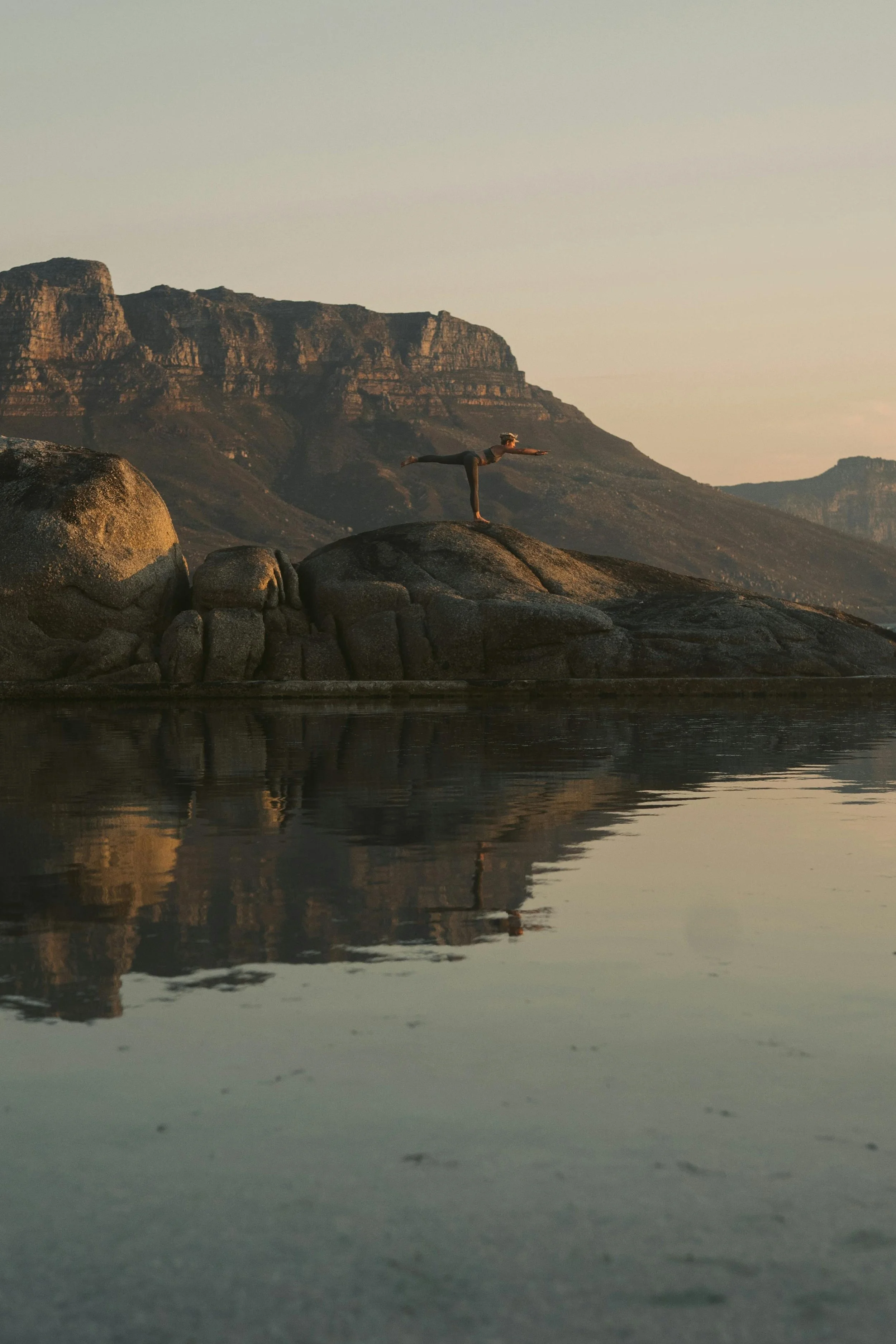 Women practicing yoga beside a calm reflective water and mountains.