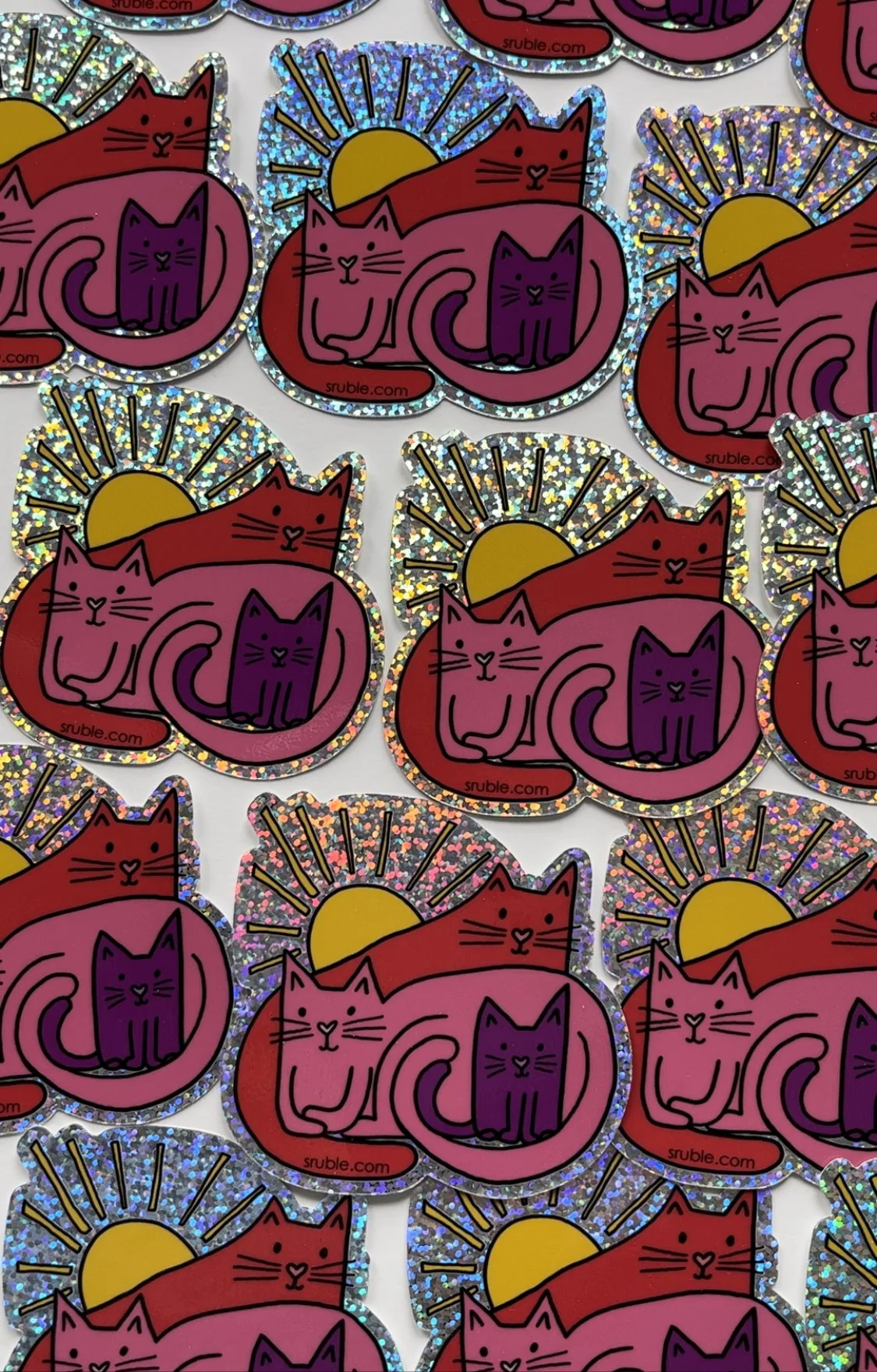 lots of stickers showing a family of kitties (big red sitting up in back, big pink laying down in middle, and small purple kitty in front, with the sun behind them, and glitter as a border and around the sun