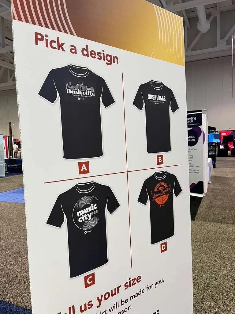 A sign with four T-shirt designs labeled A, B, C, and D, inviting viewers to pick a design in live screen printing event.