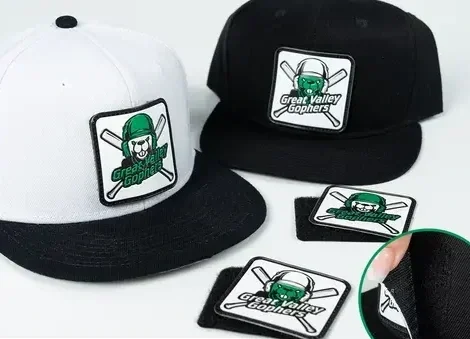 Two baseball caps, one white with a black brim and one black, both with 'Great Valley Gophers' logo, along with patches and stickers featuring the gopher mascot.