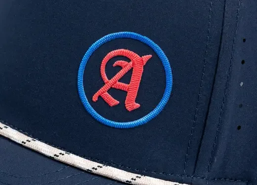 Close-up of a navy blue baseball cap with a red and blue embroidered logo of a stylized letter 'A' inside a blue circle.