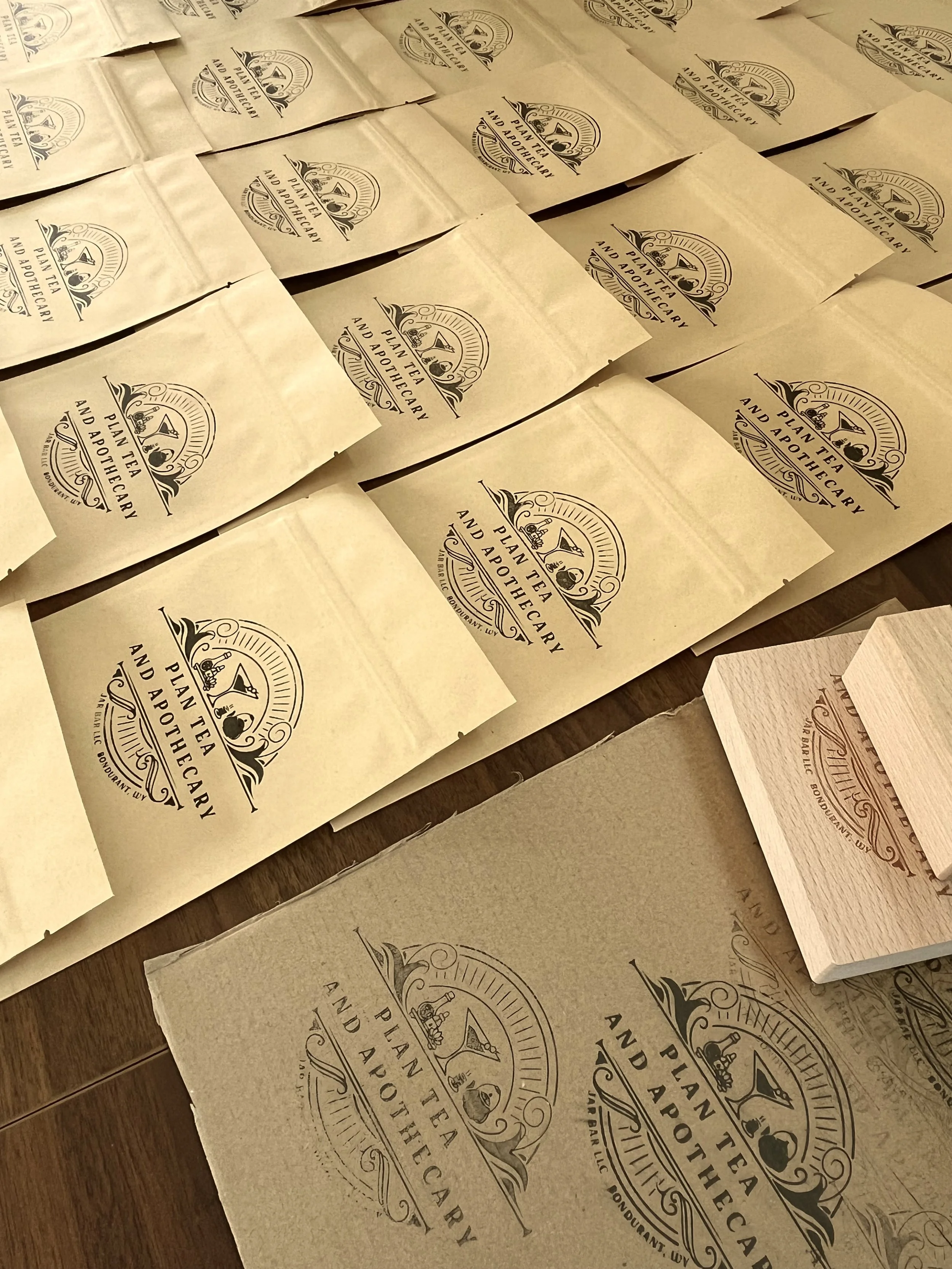 Multiple heat sealable bags stamped with a logo reading 'Plan Tea and Apothecary' printed on them, laid out on a table.