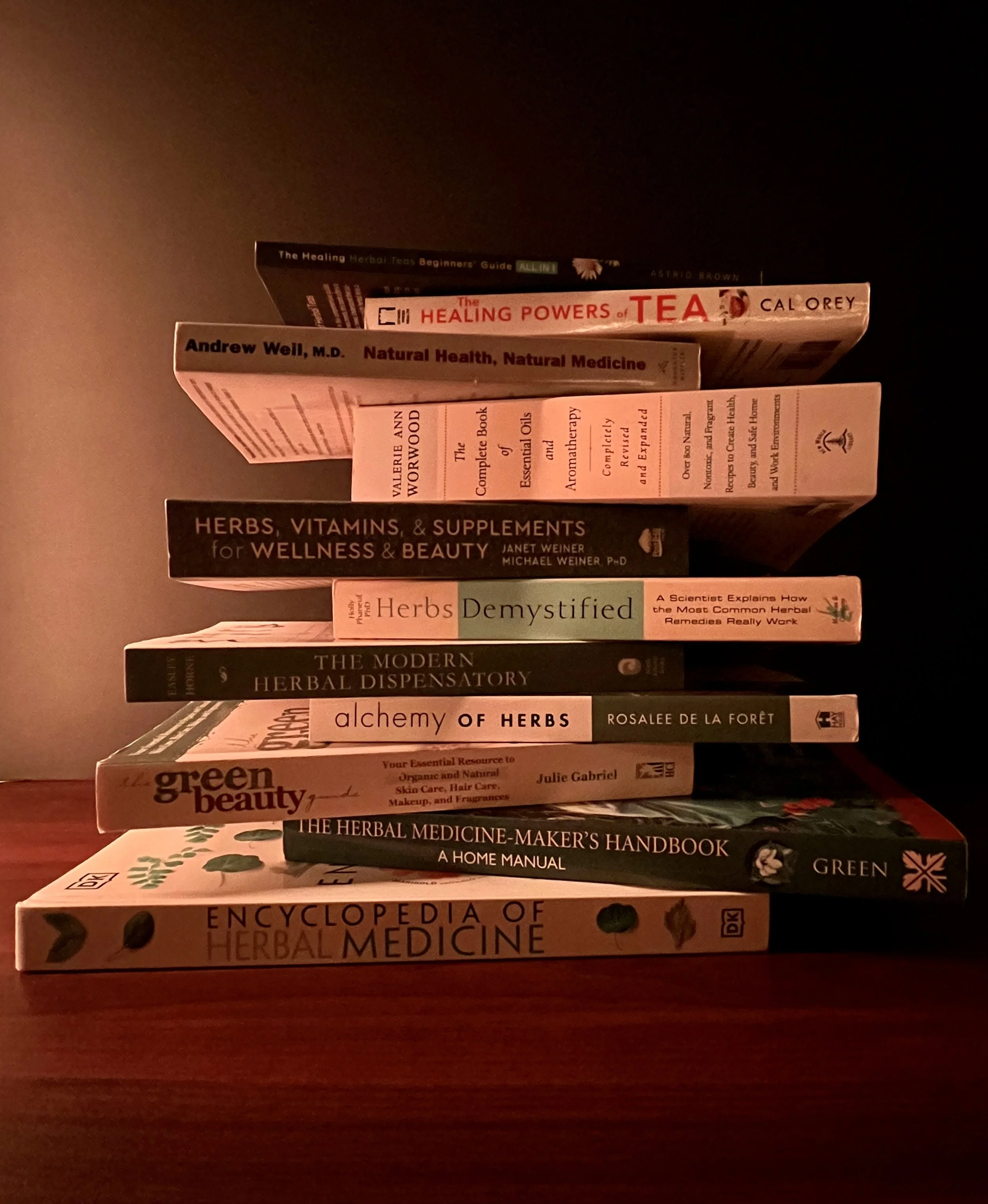 Stack of health, wellness, and herbal medicine books on a wooden surface, featuring titles on herbal therapy, natural health, and herbal medicine.