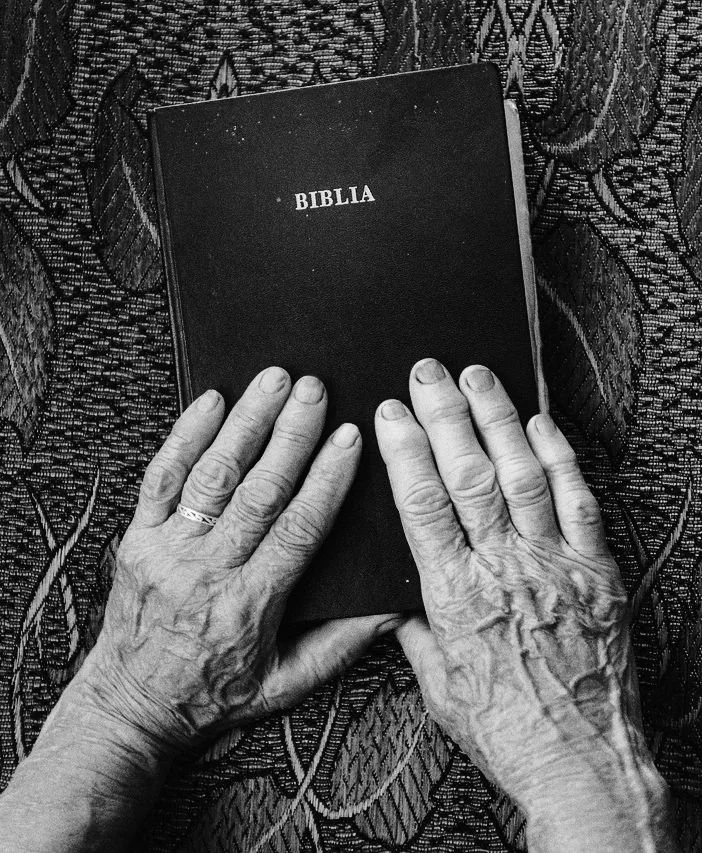 Mãos idosas a segurar uma Bíblia antiga em fotografia a preto e branco, representando as raízes, os valores e a herança familiar.