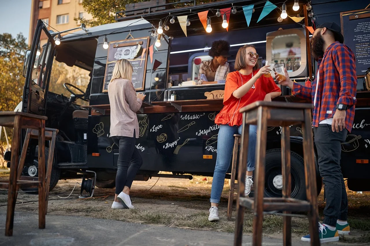 People enjoying drinks at a food truck outdoor event with string lights and festival decorations.