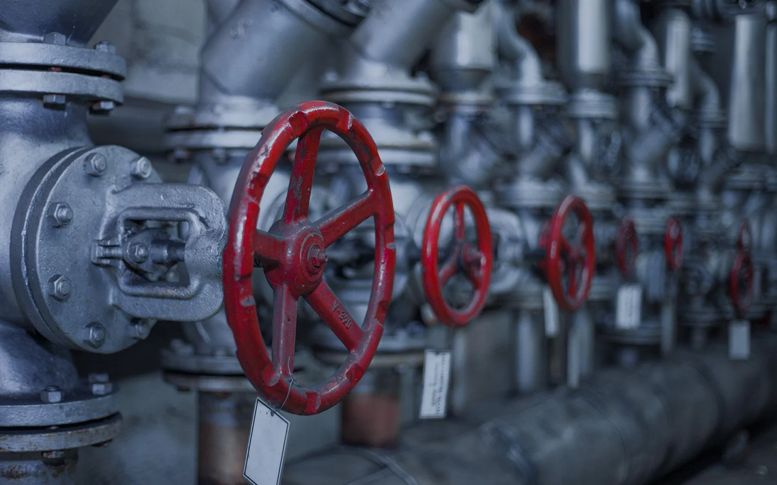 Industrial valve assembly with multiple red handwheels inside a mechanical room