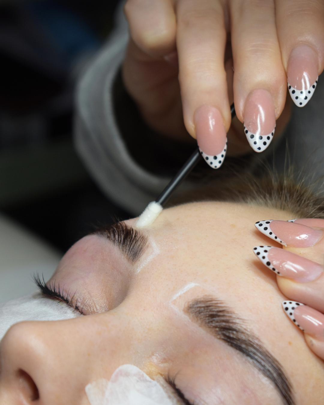 A person with manicured nails receiving a facial treatment with a cotton swab on their forehead.