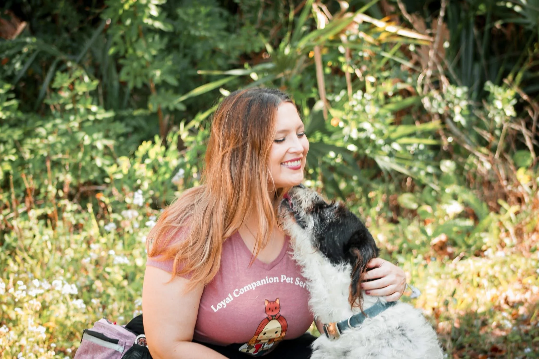Woman petsitter smiling as dog licks her face outside