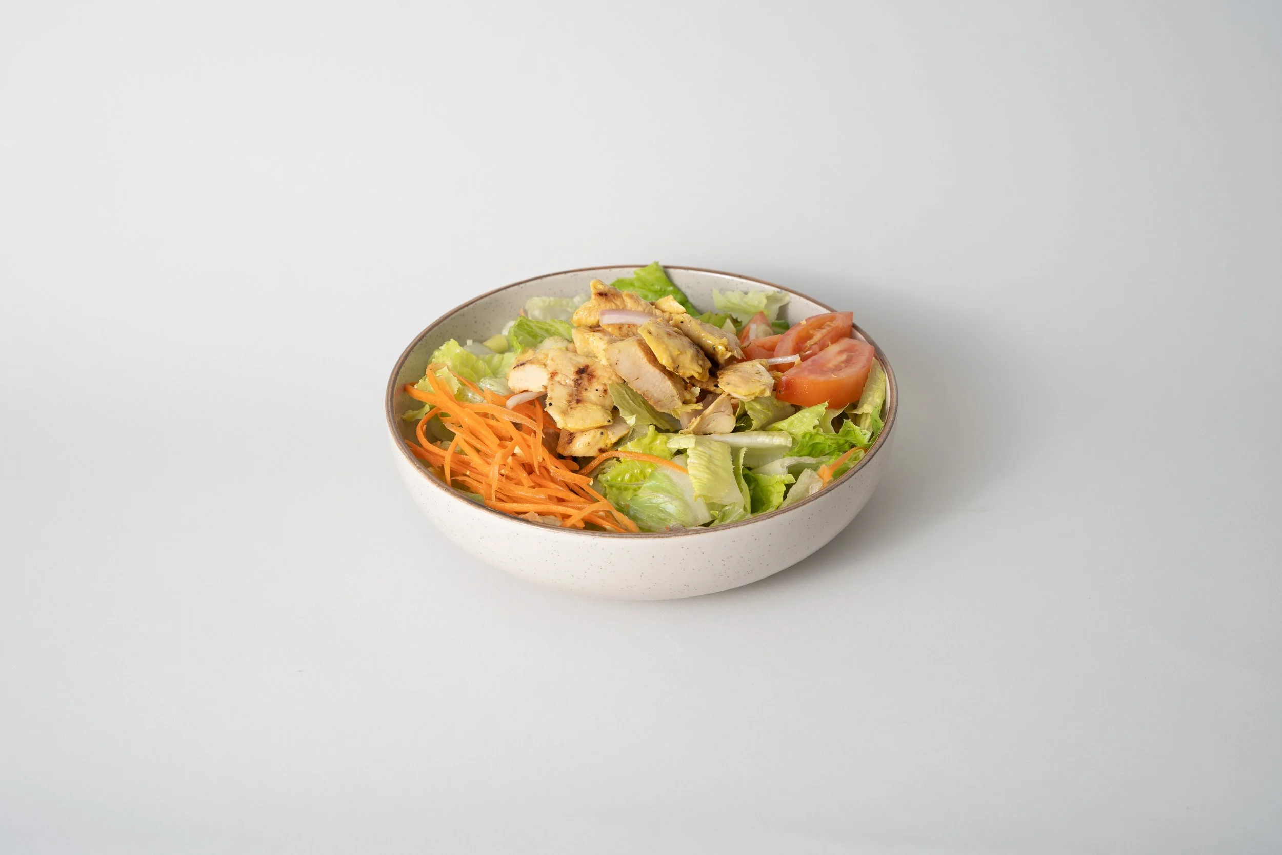 Bowl of fresh salad with lettuce, cherry tomatoes, shredded carrots, grilled chicken slices, and red onions on a white background.