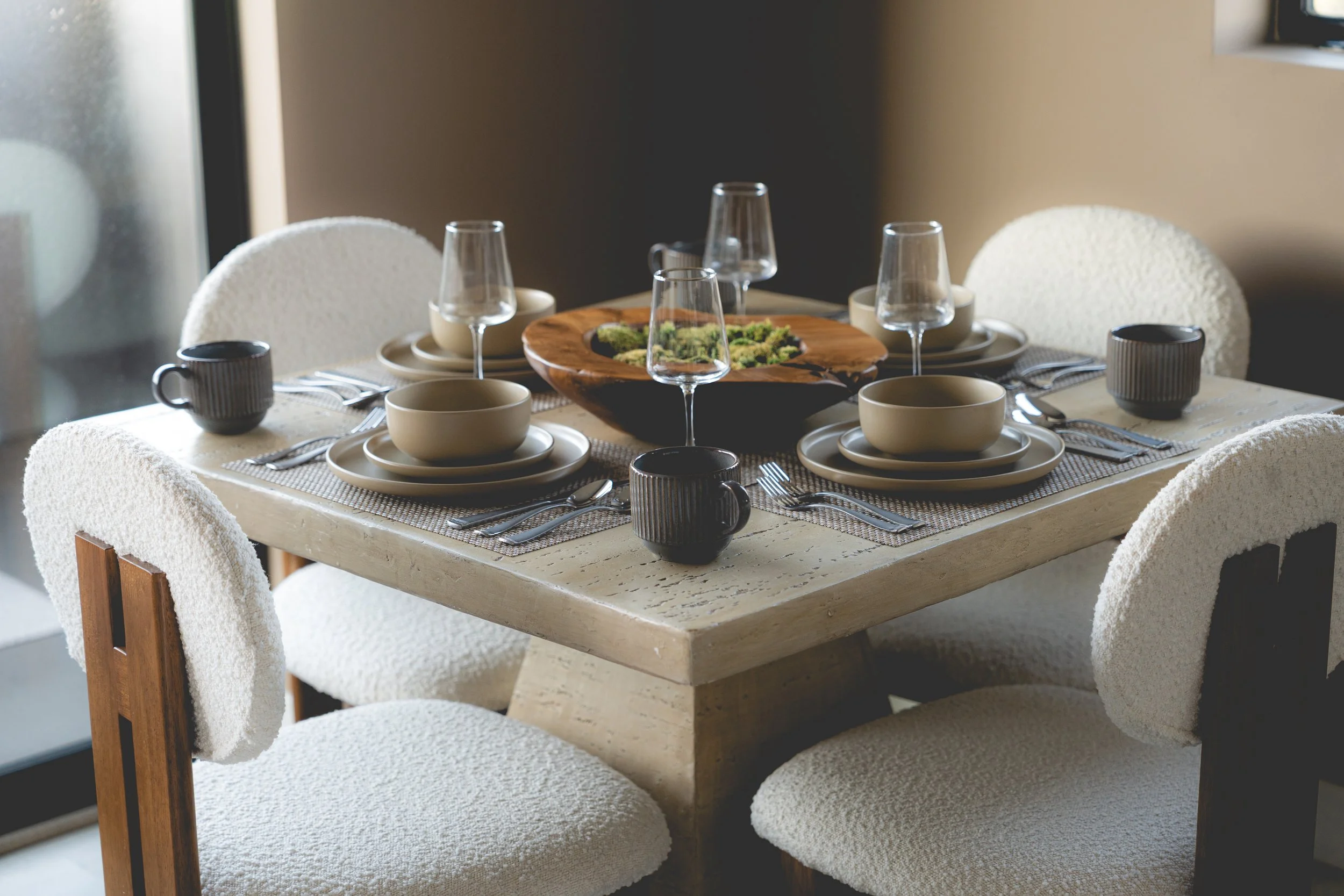 A dining table set for six people with dishes, wine glasses, mugs, and utensils, and a wooden serving tray with a green salad in the center.