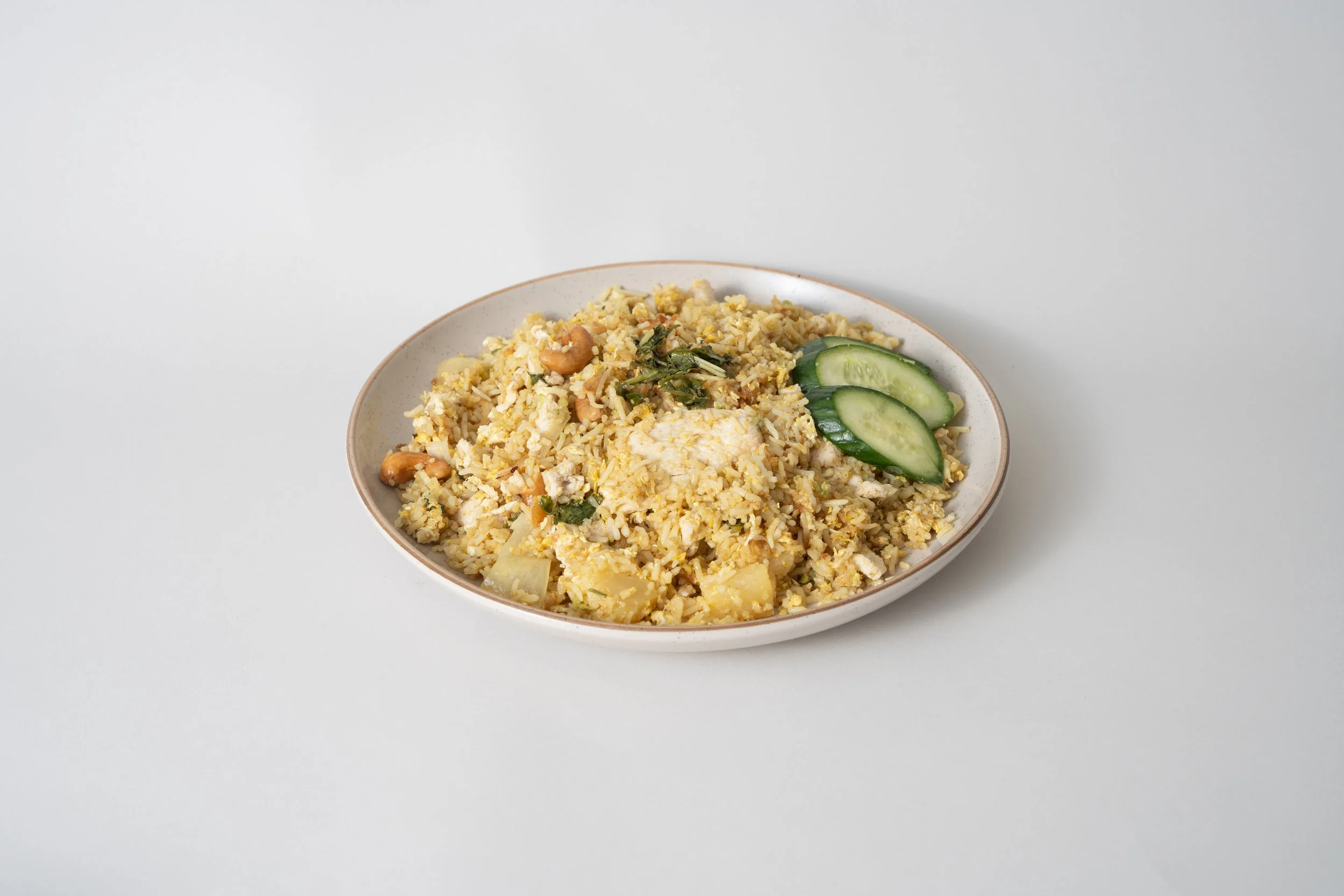 Plate of fried rice with vegetables and cucumber slices on the side.