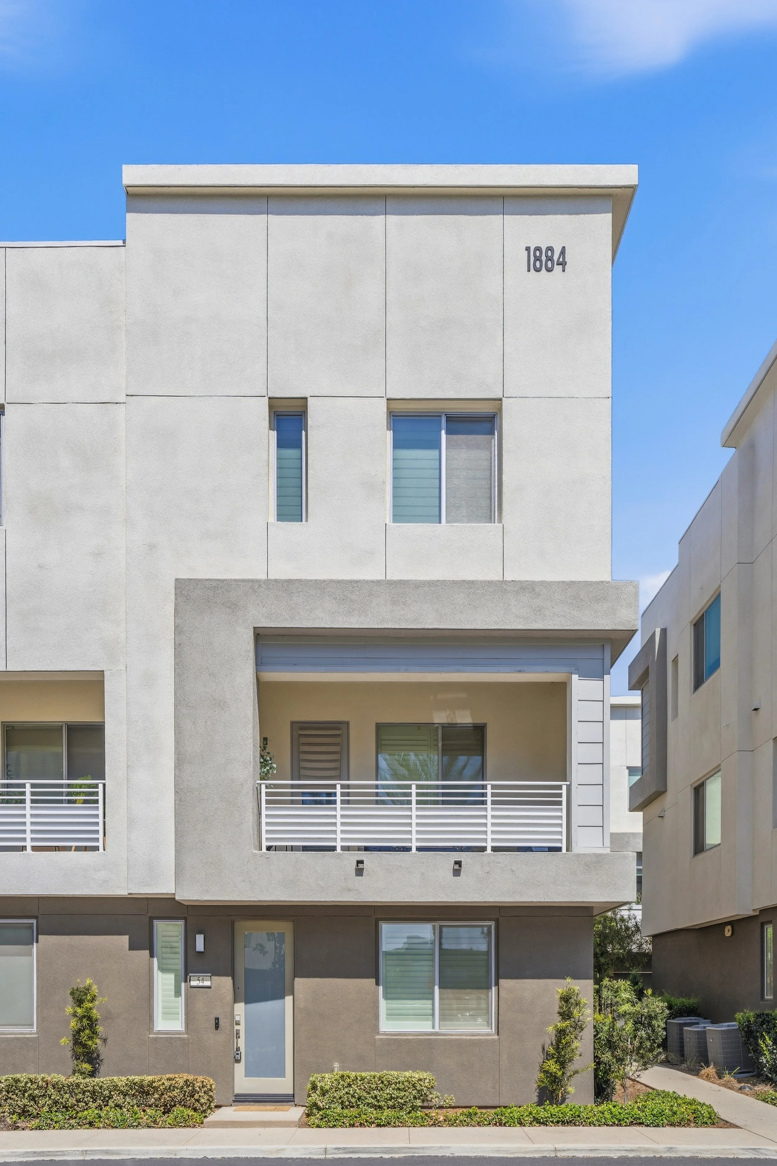Modern multi-story residential building with stucco exterior, small balcony, and clear blue sky.