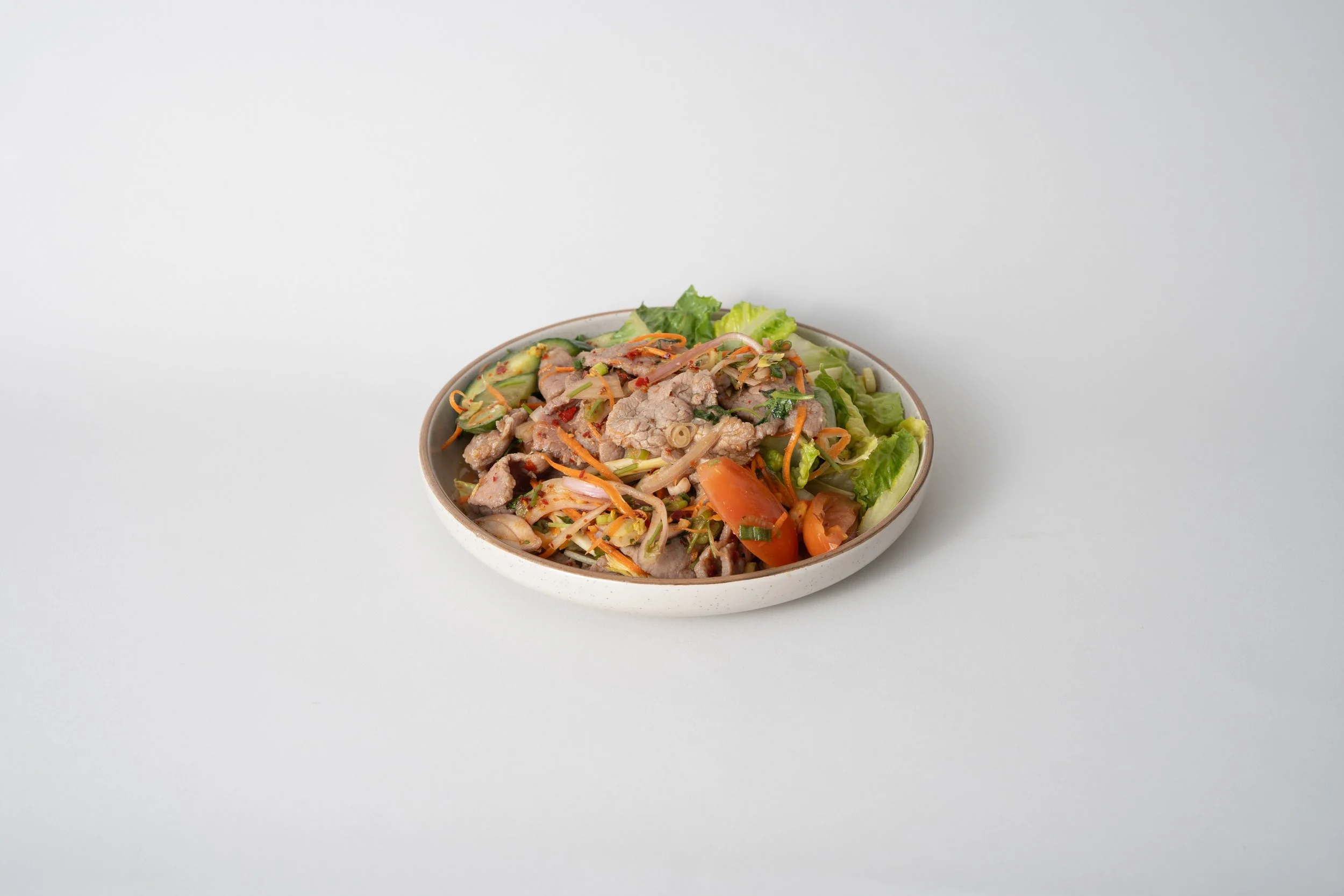 Bowl of Asian stir-fried vegetables and sliced pork on a white surface