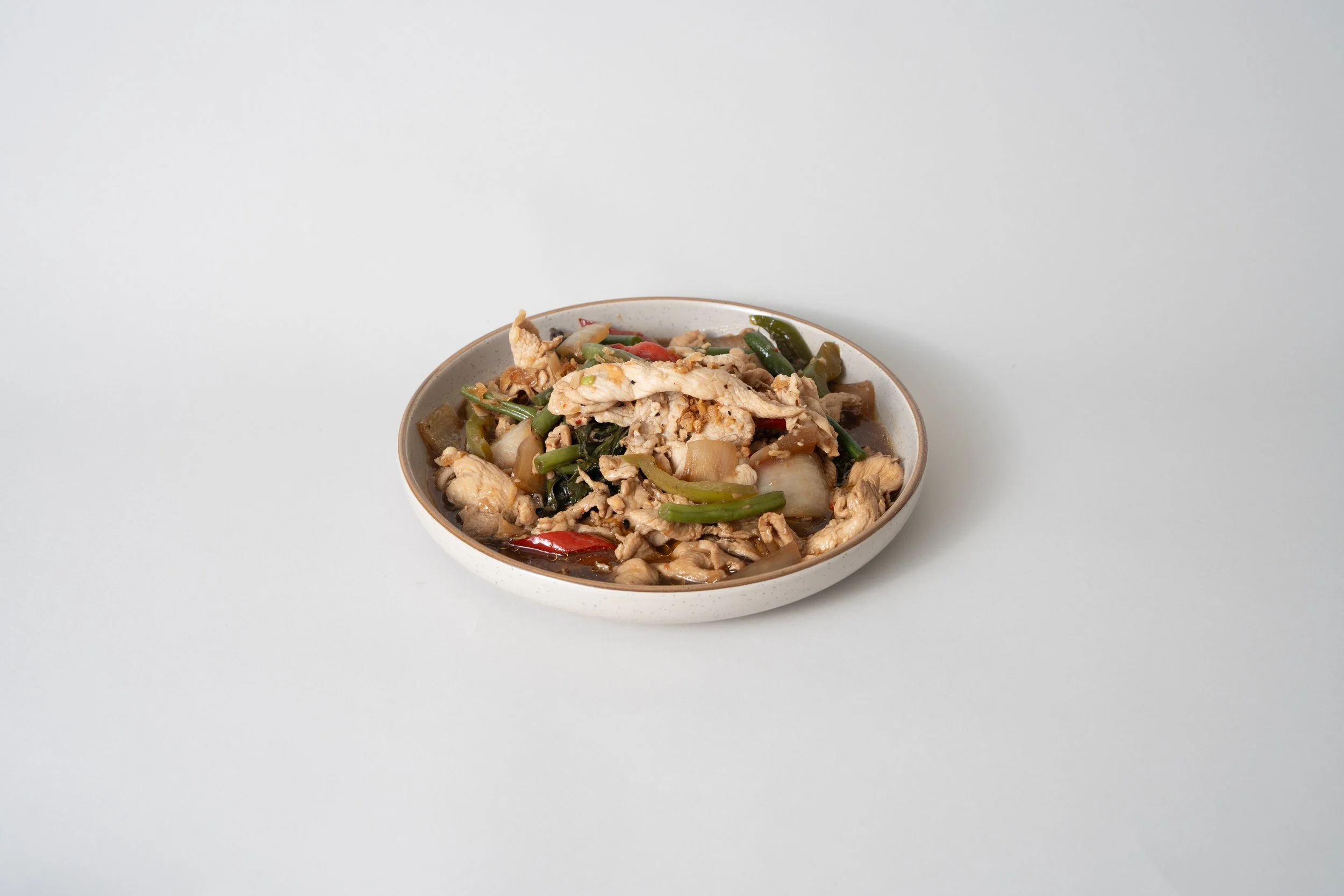 A bowl of stir-fried vegetables and chicken on a plain white background.