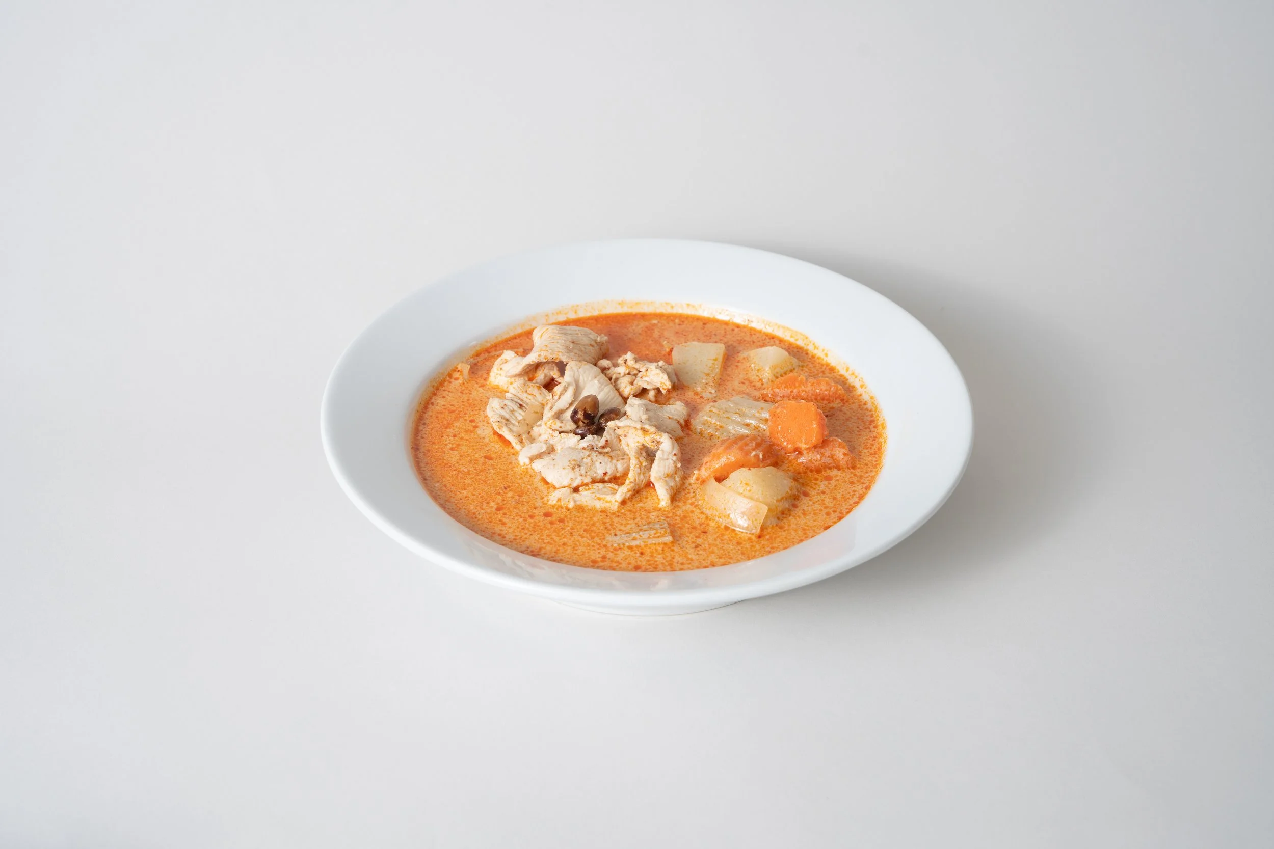 A white bowl of chicken and vegetable soup on a plain white surface.