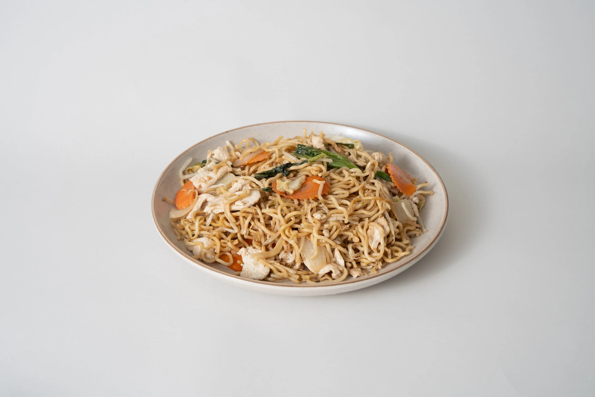 Plate of cooked ramen noodles with vegetables and shredded chicken on a white background.