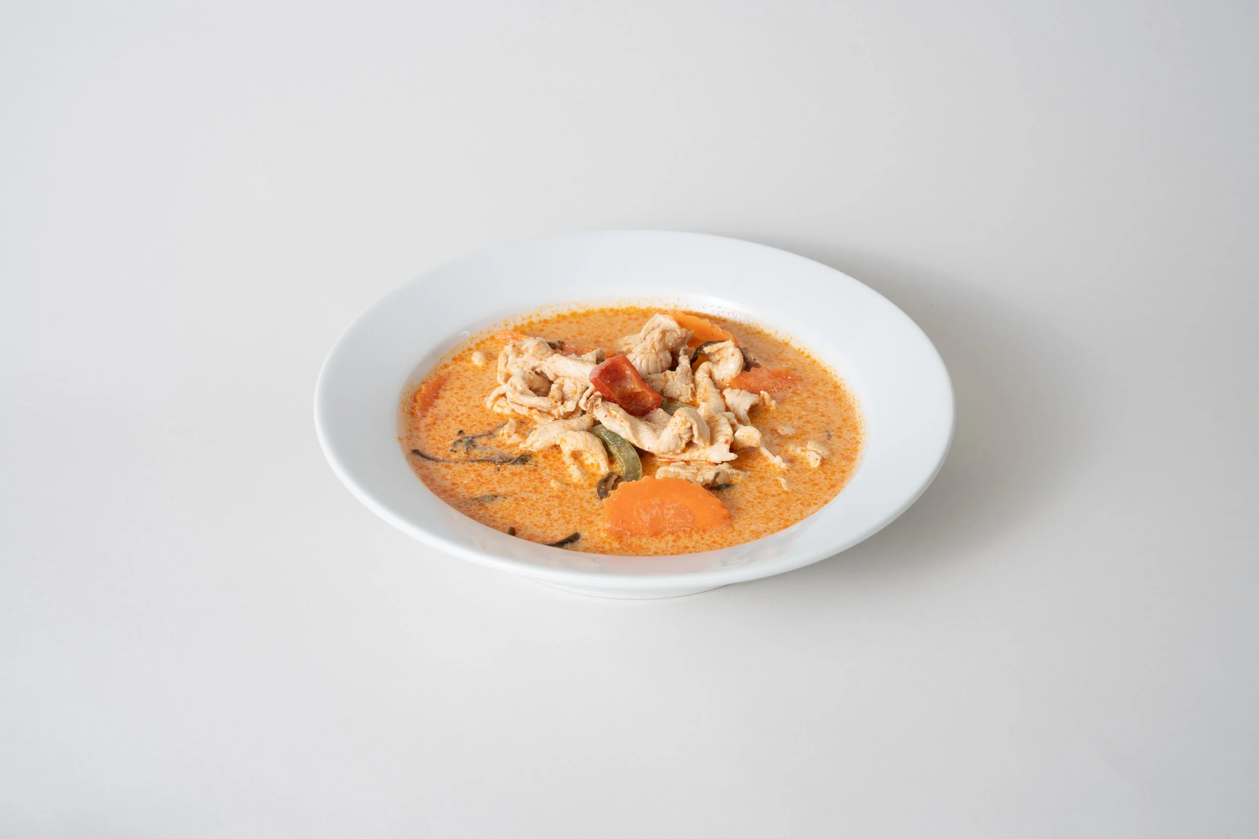 Bowl of Thai curry with chicken, vegetables, and orange sauce.