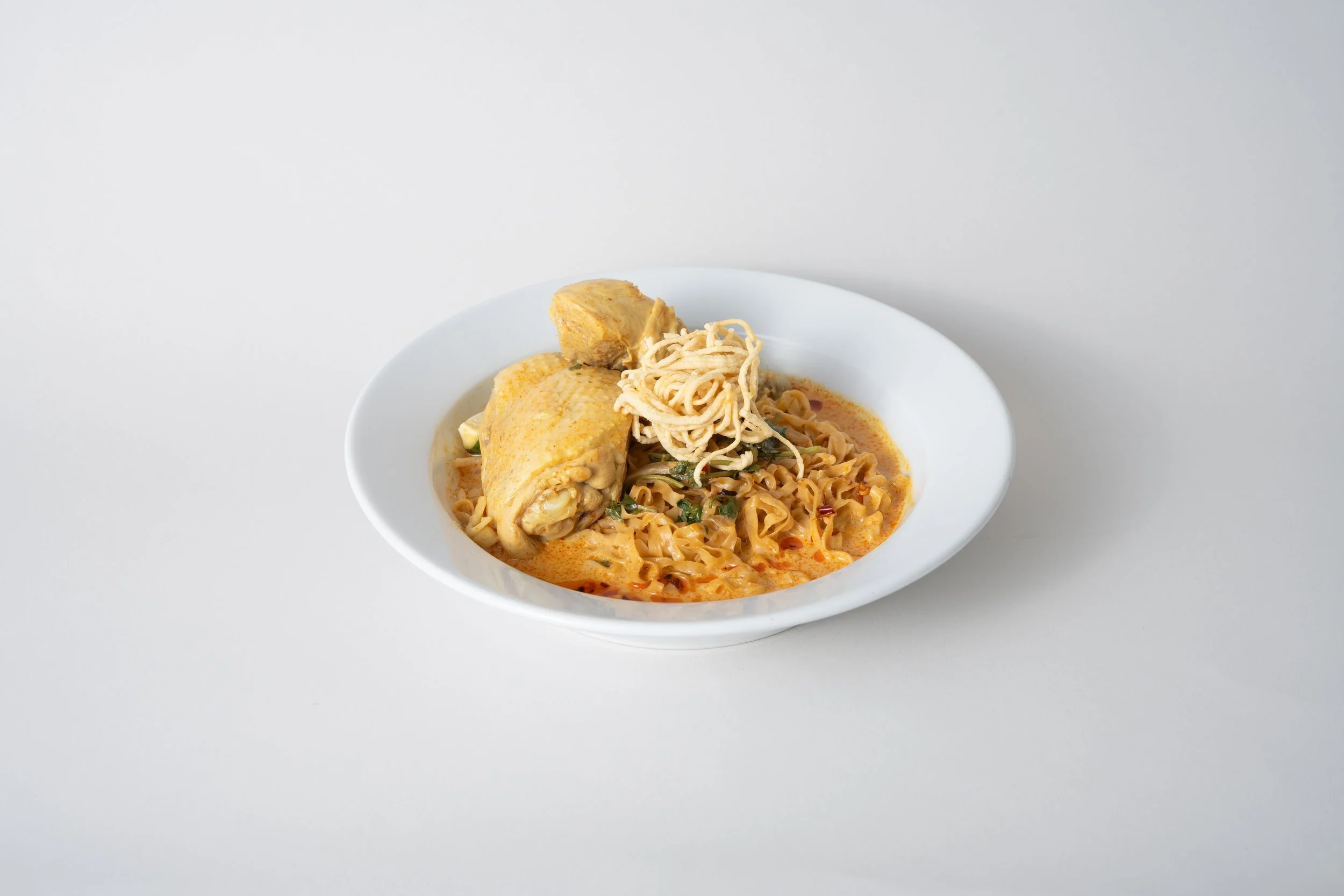 Bowl of chicken noodle soup with chicken pieces, noodles, vegetables, and garnished with fried noodles on top.