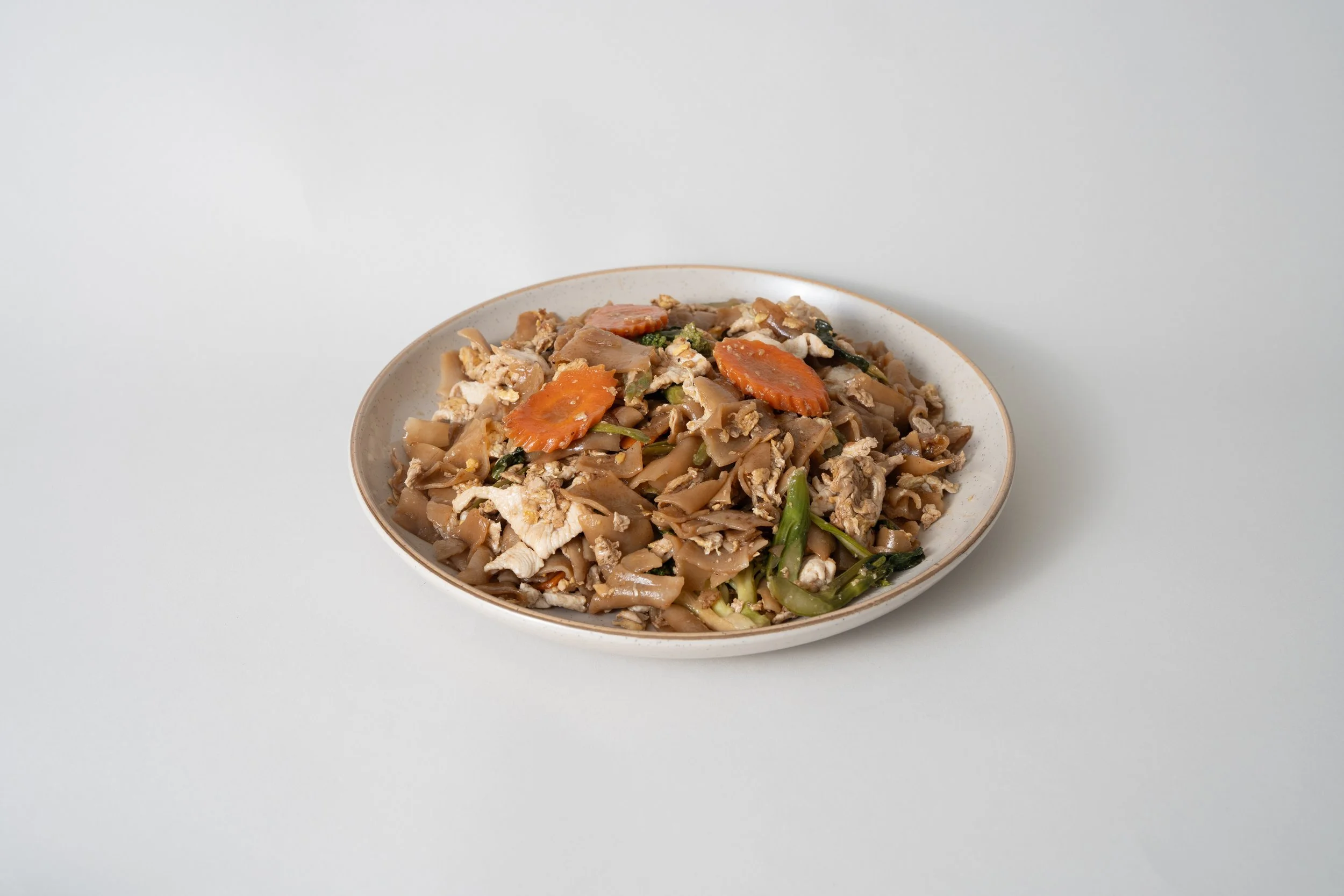 Plate of stir-fried noodles with vegetables and chicken on a white surface.